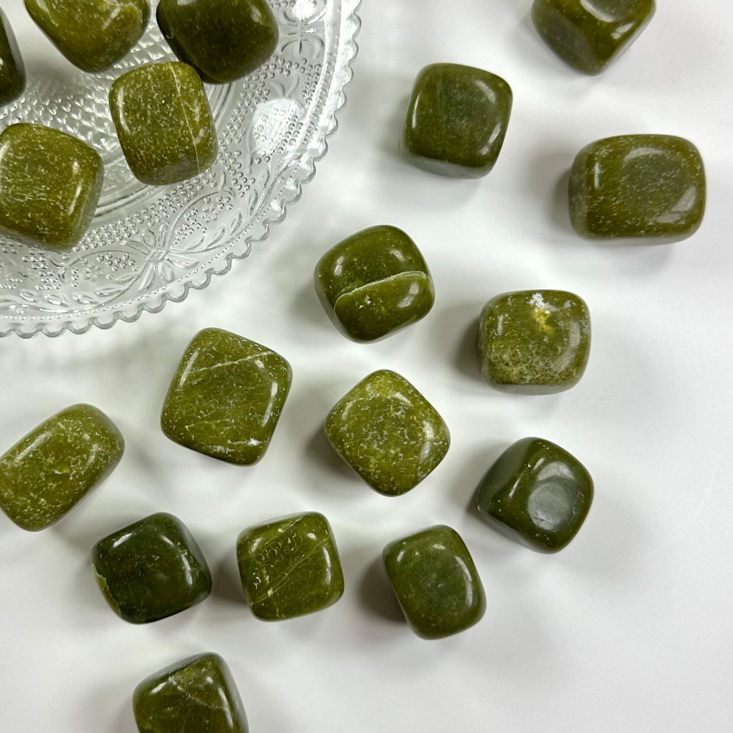 Grøn jade lommesten spredt på en hvid overflade ved siden af en mønstret glasskål.