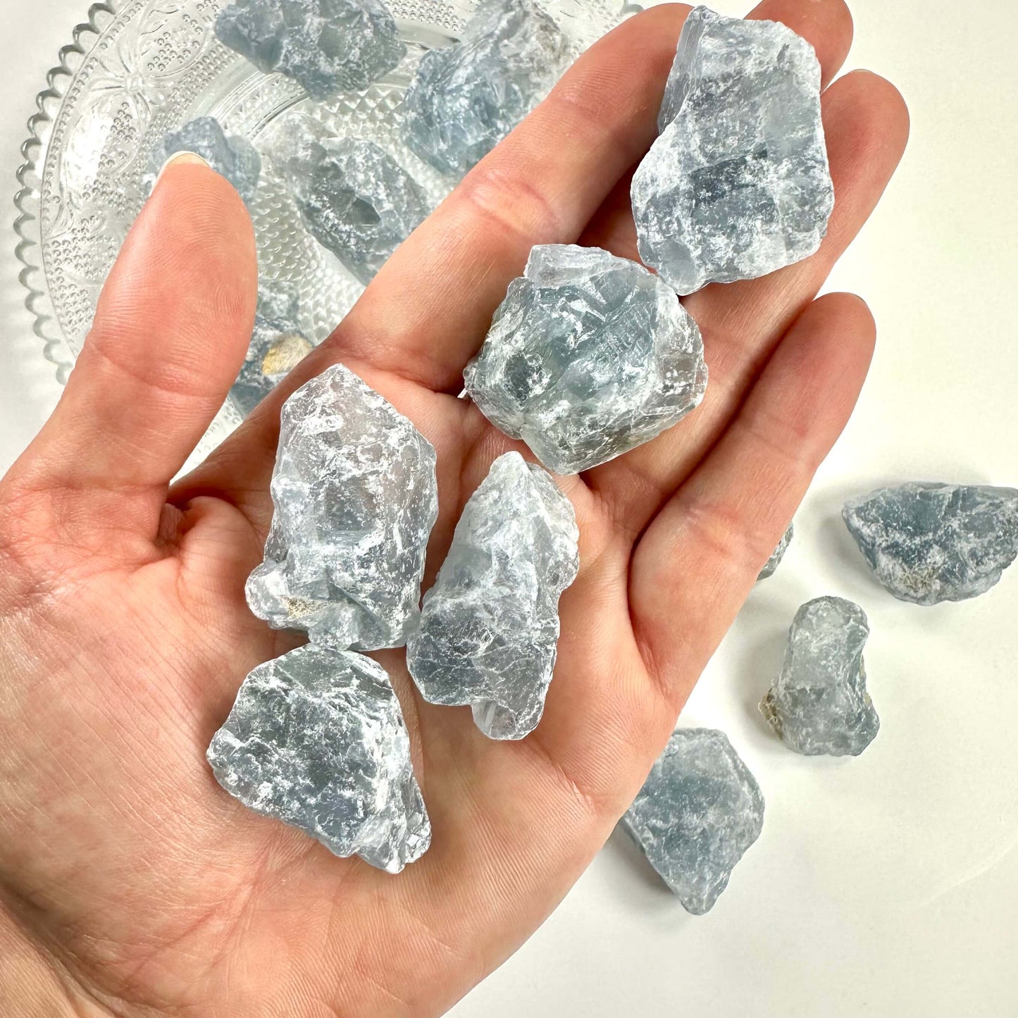 Person holder flere stykker rå Celestit i hånden.