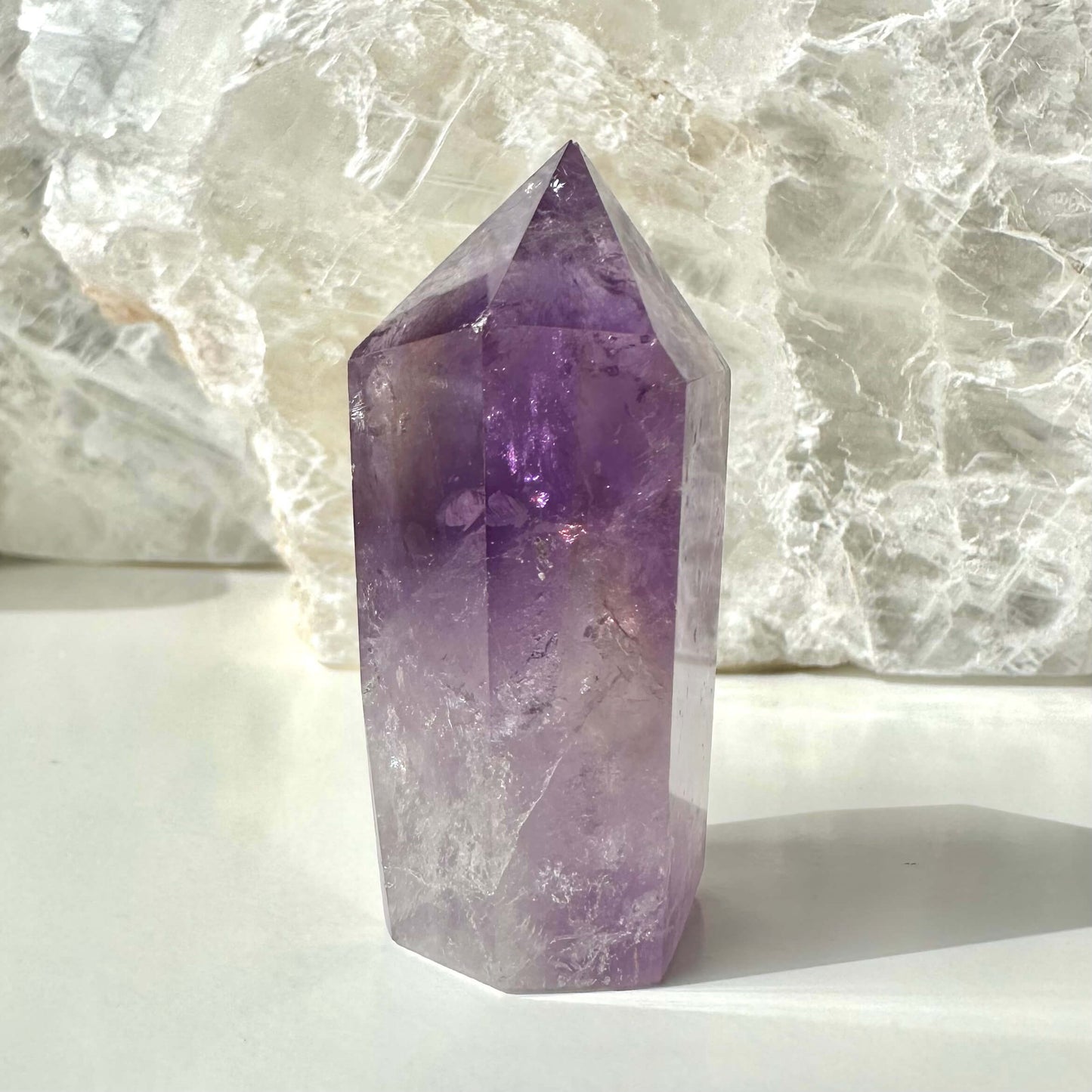 En ametrin spids krystal står oprejst foran en lys baggrund, der fremhæver dens lilla og klare nuancer.