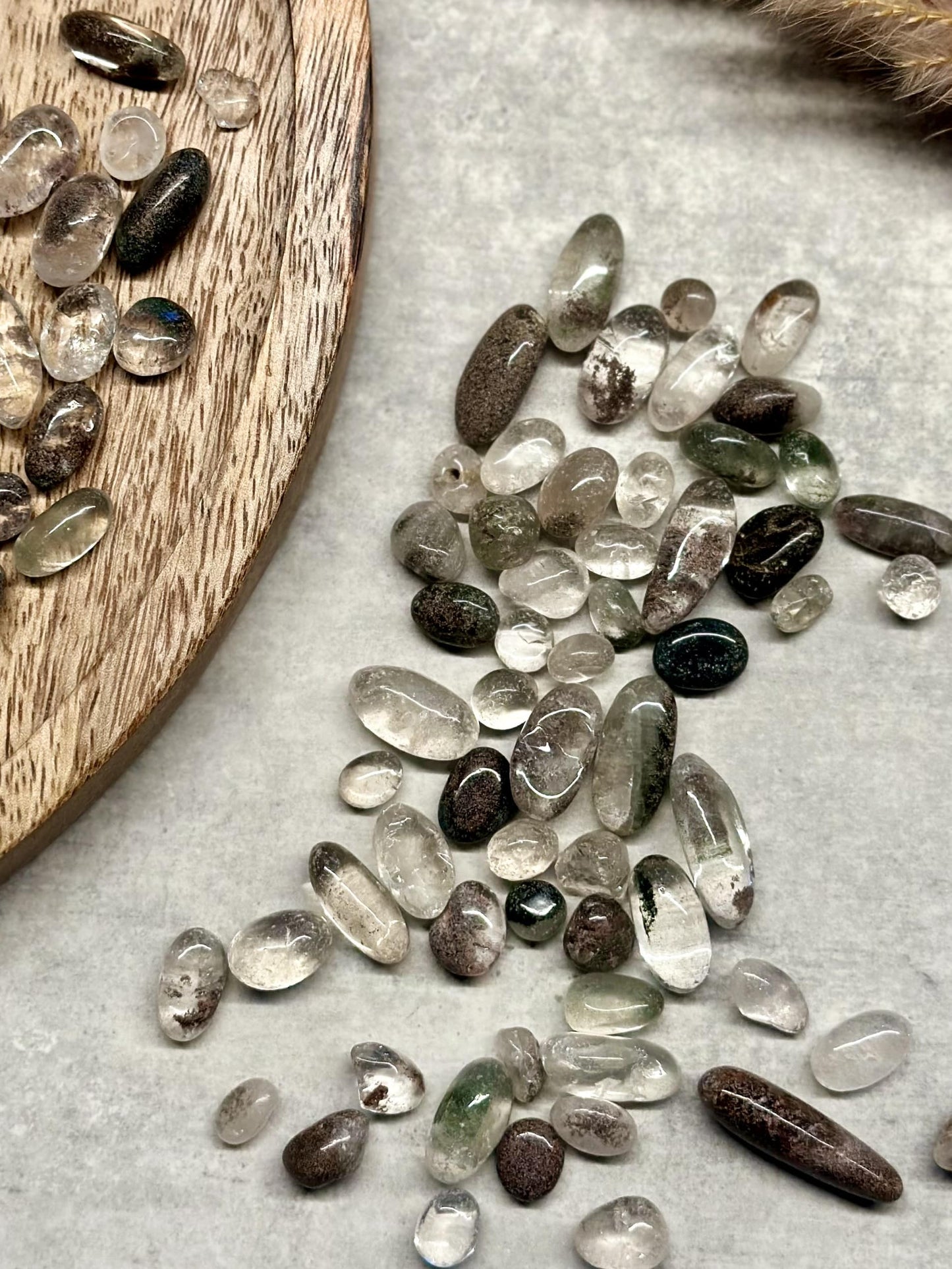 Klare og flerfarvede Fantomkvarts chips spredt på en beige overflade og en træbakke.