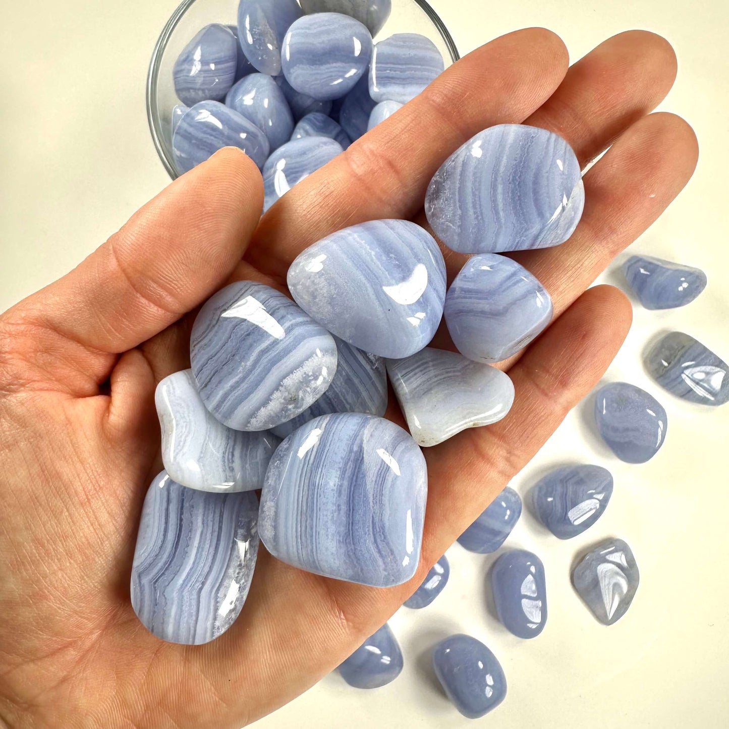 En hånd fyldt med glatte blonde agat lommesten i lyseblå nuancer.