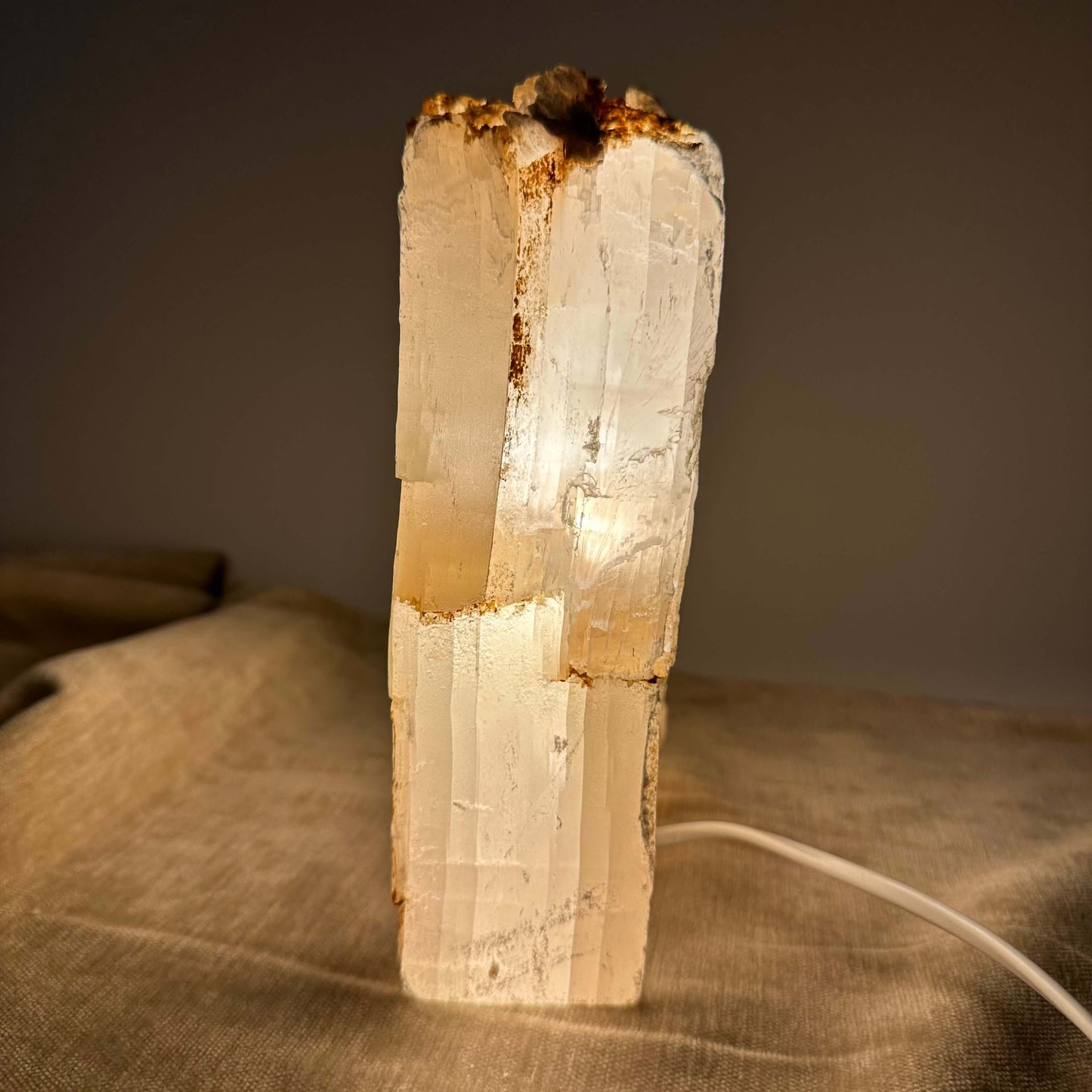 Mexicansk Selenit lampe nr 5 skinner varmt lys på en beige overflade med en ledning ved siden af.