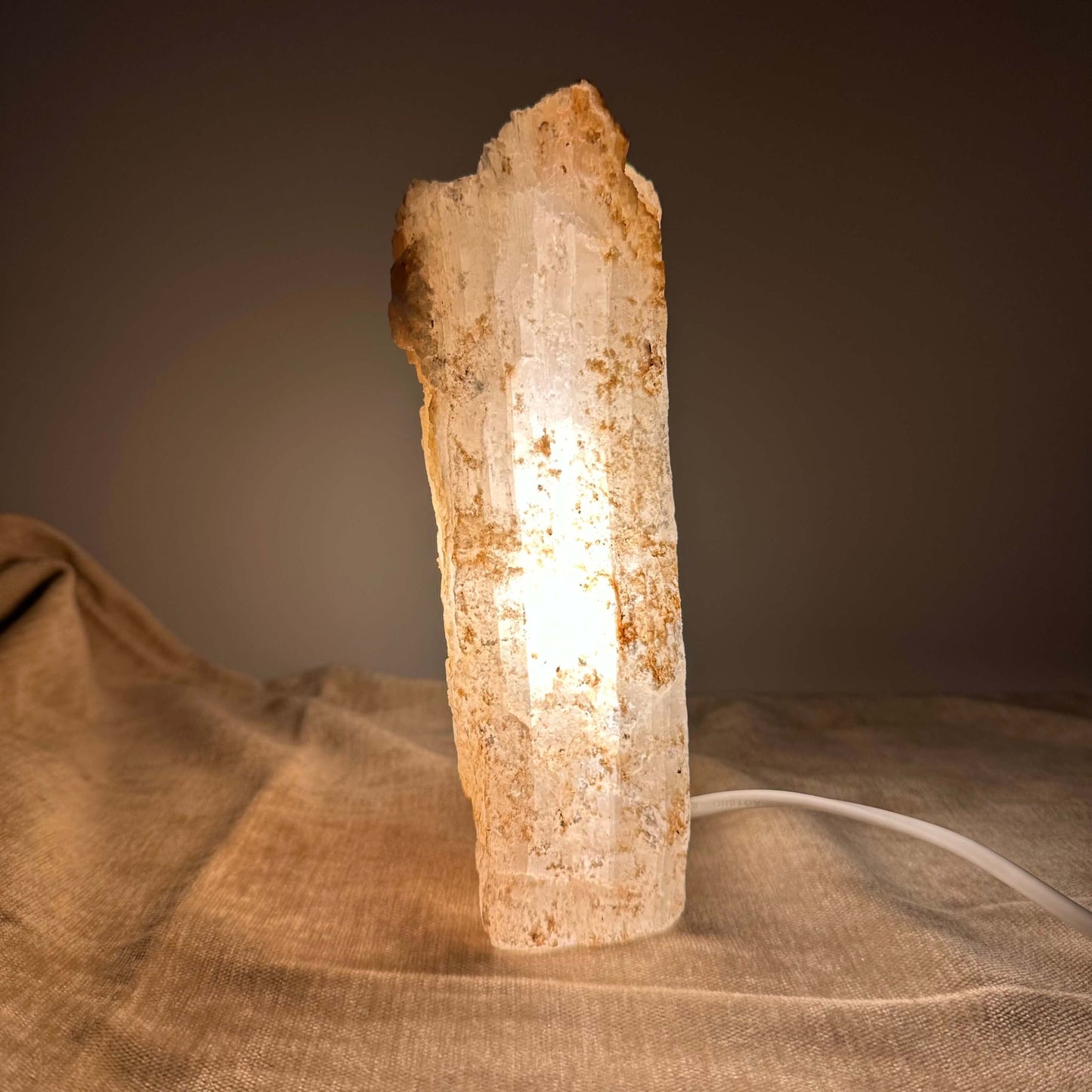 Mexicansk Selenit lampe nr 45 lyser på et bord med blødt, varmt lys. Lampen står på et stofdække underlag.