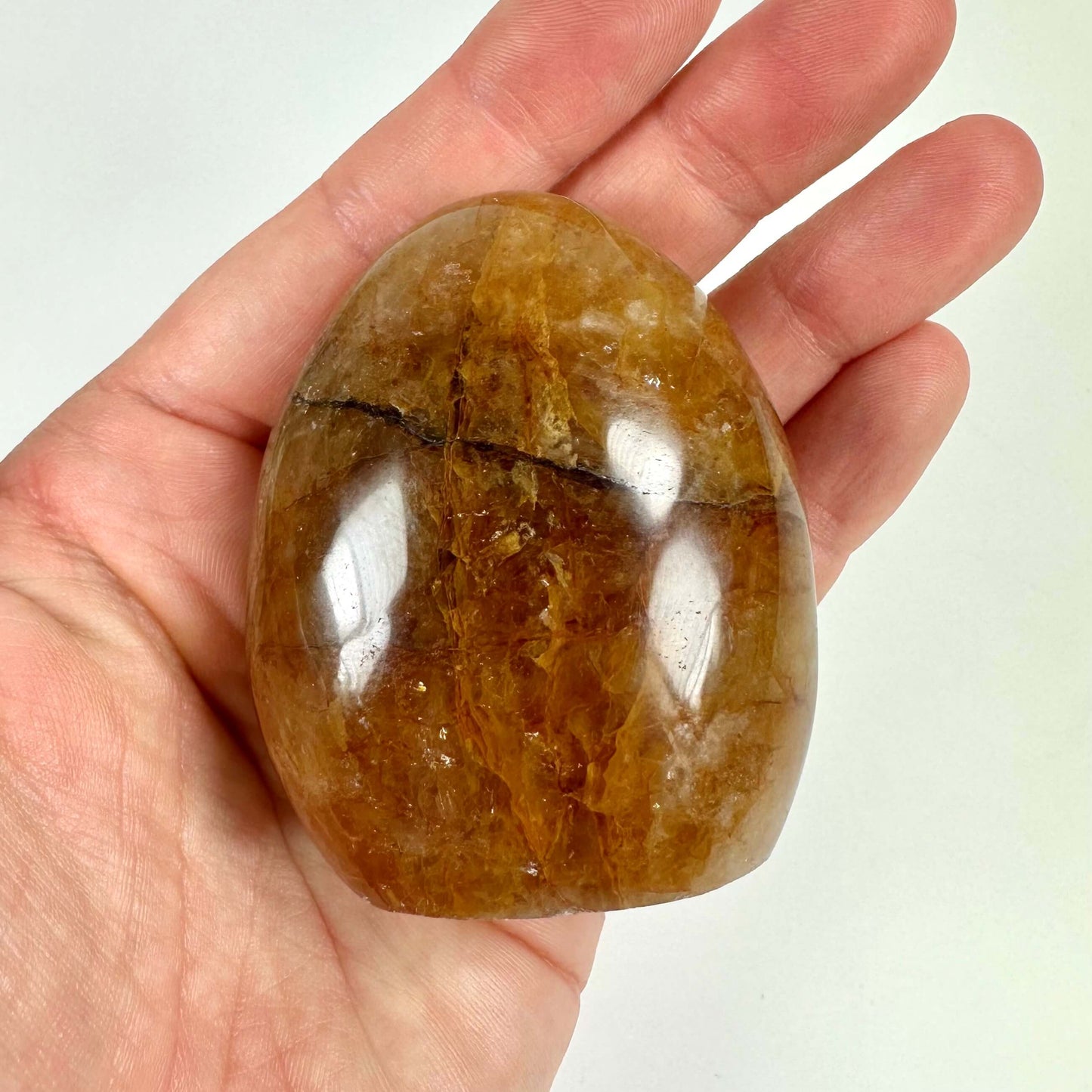 En hånd holder en glat, poleret Golden Healer fri form krystal med gyldne toner.