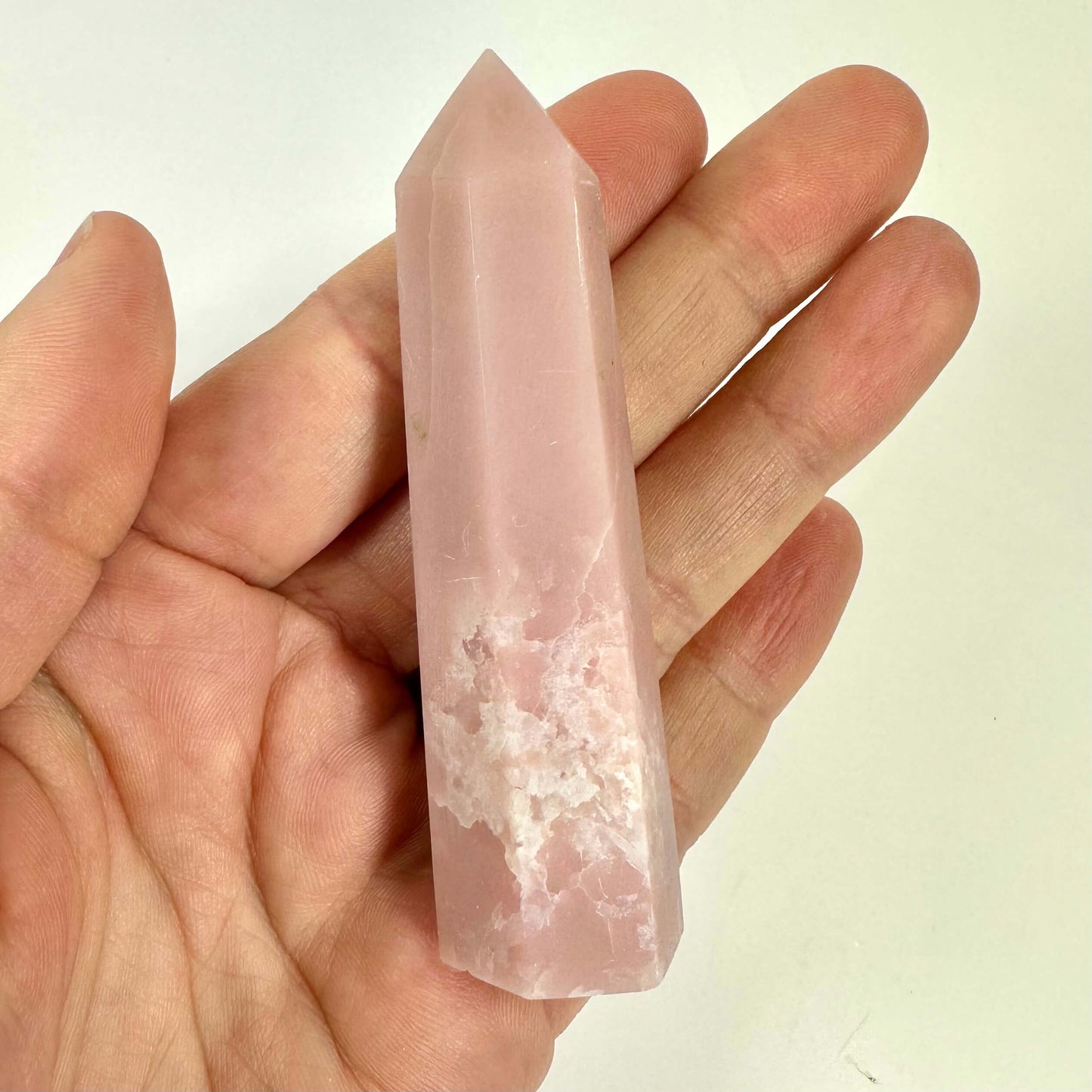 En person holder et Pink opal tårn i hånden mod en lys baggrund.