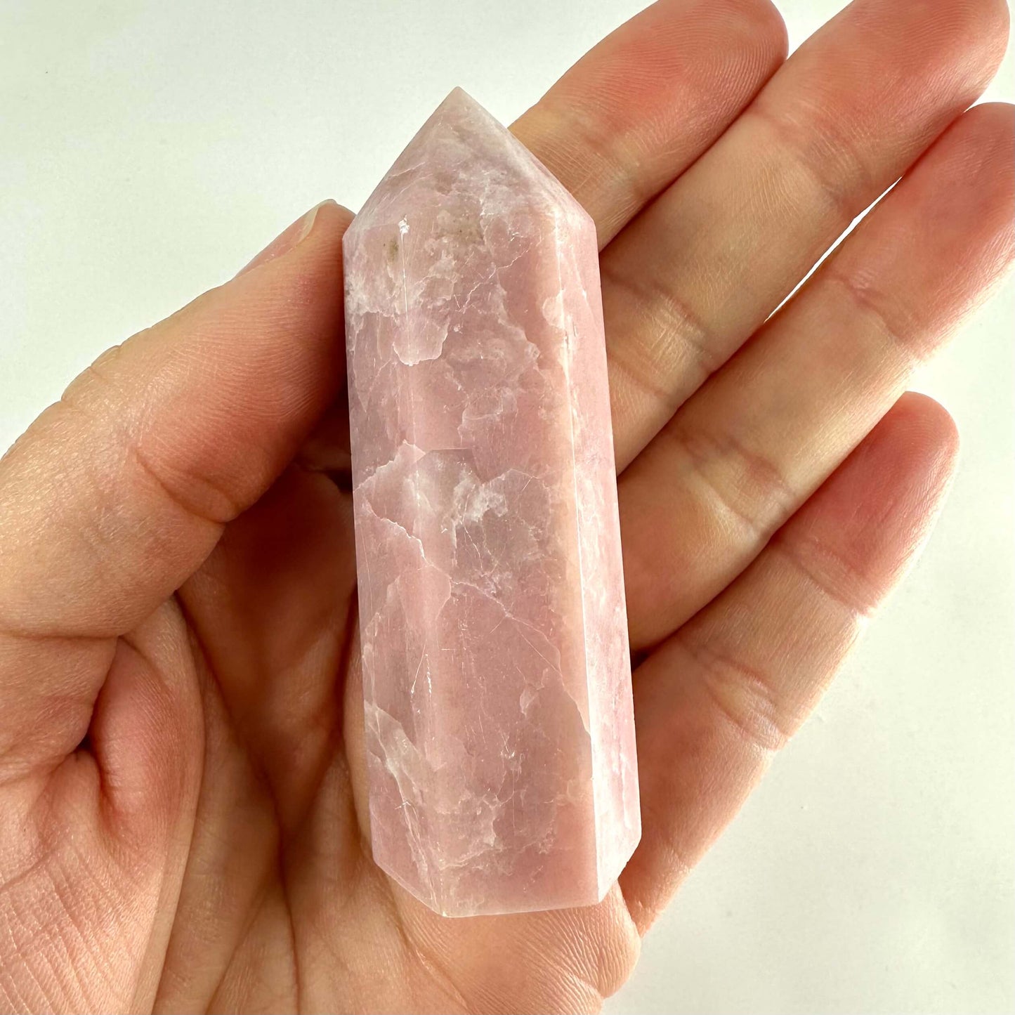 Hånd holder et glat Pink opal tårn mod en lysegrå baggrund.