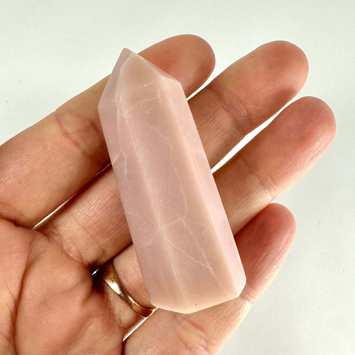 Hånd, der holder et pink opal tårn med en spids top på en neutral baggrund.