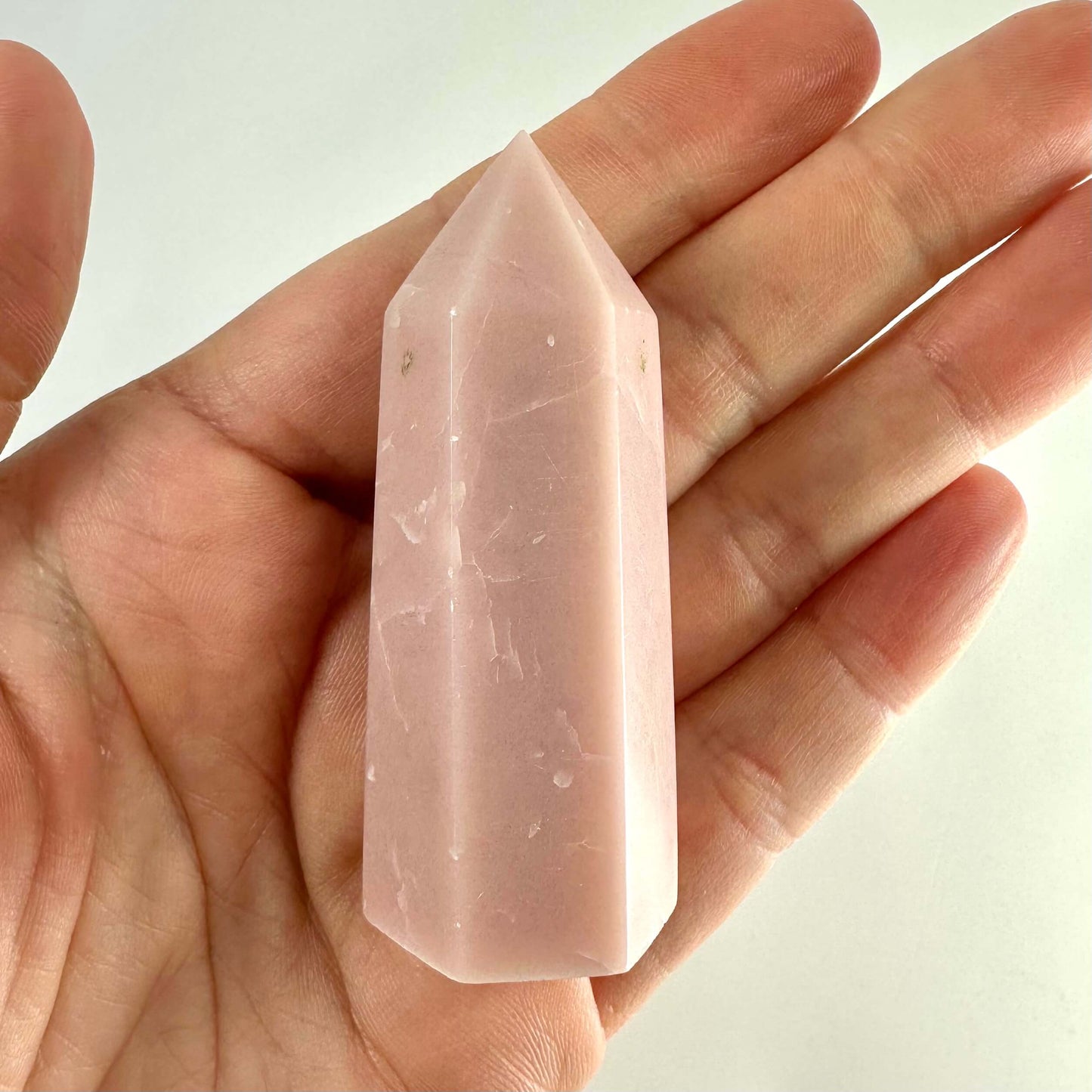 En hånd holder et Pink opal tårn mod en lys baggrund.