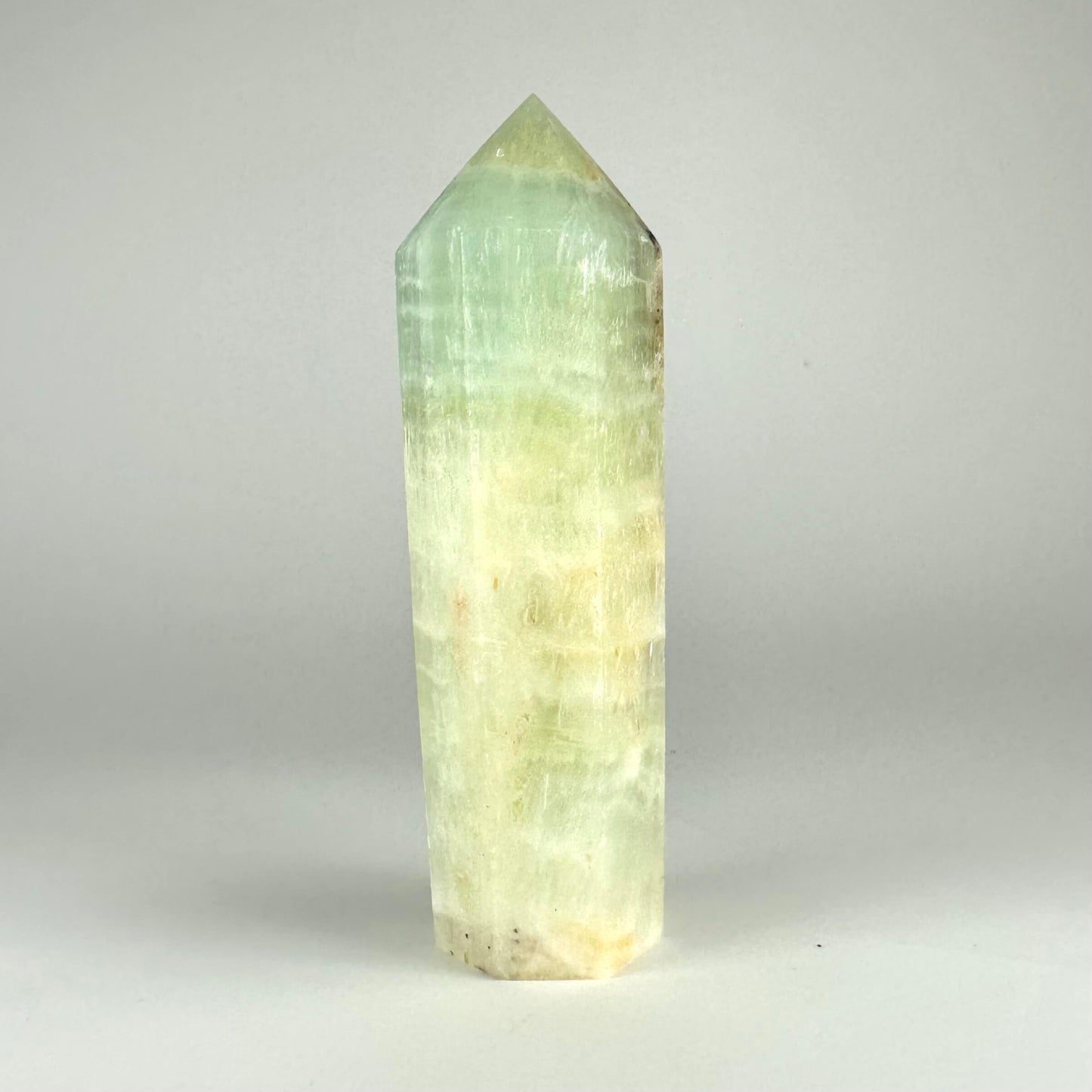 Pistacie calcit tårn mod en neutral grå baggrund, viser lysegrønne og hvide toner i en poleret, spids form.