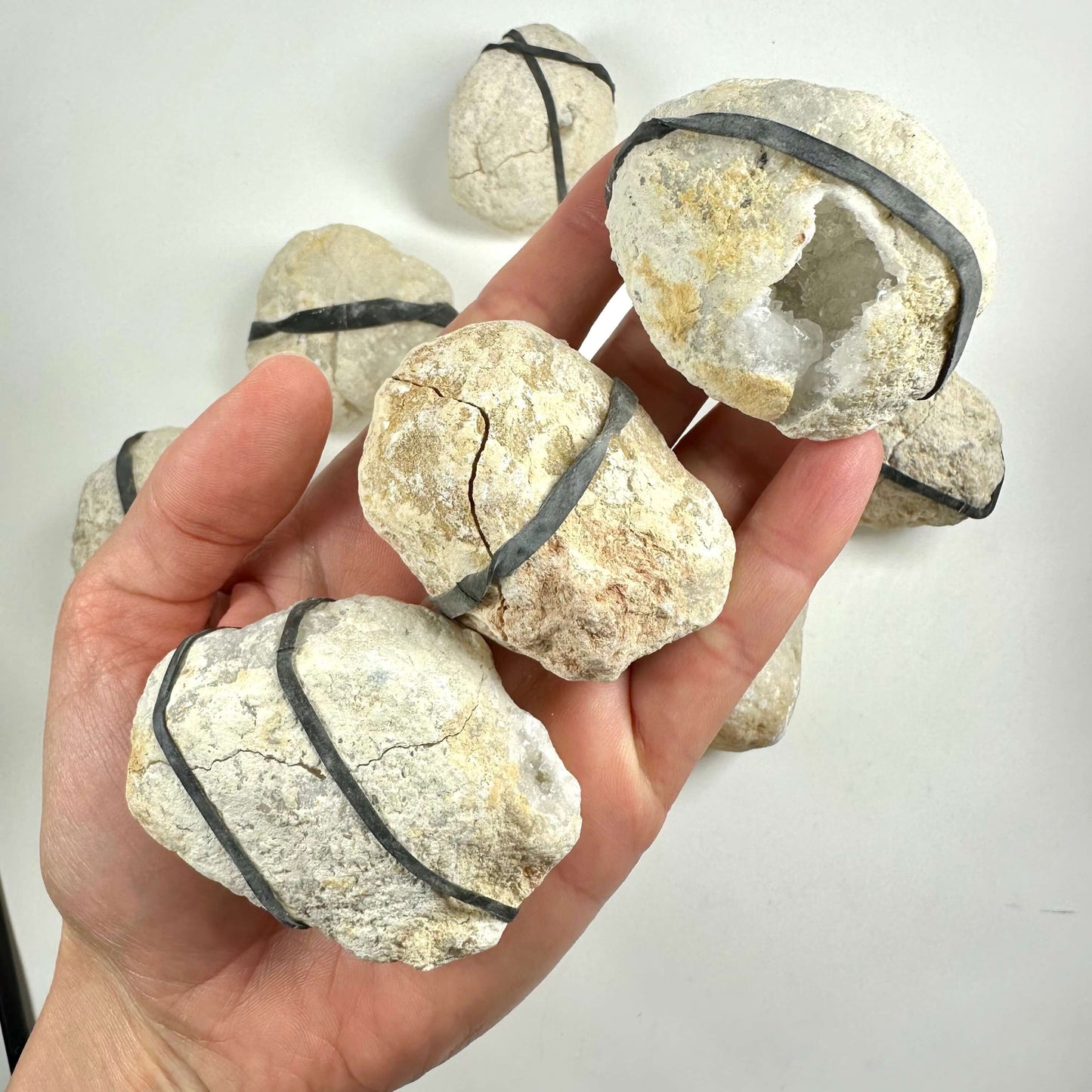 Hånd holder kvartsgeoder med elastikker. Nogle er lukkede, andre åbne, der viser krystaller.