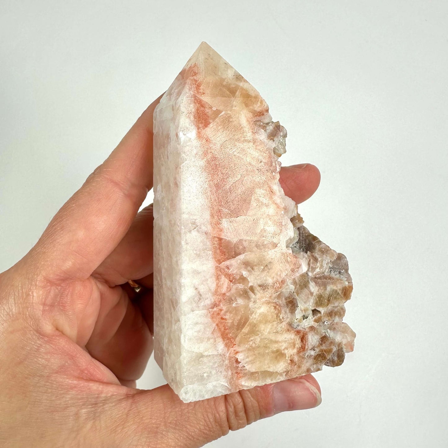 Hånd, der holder en Calcit hundetand-krystal med en mix af hvide og beige nuancer.