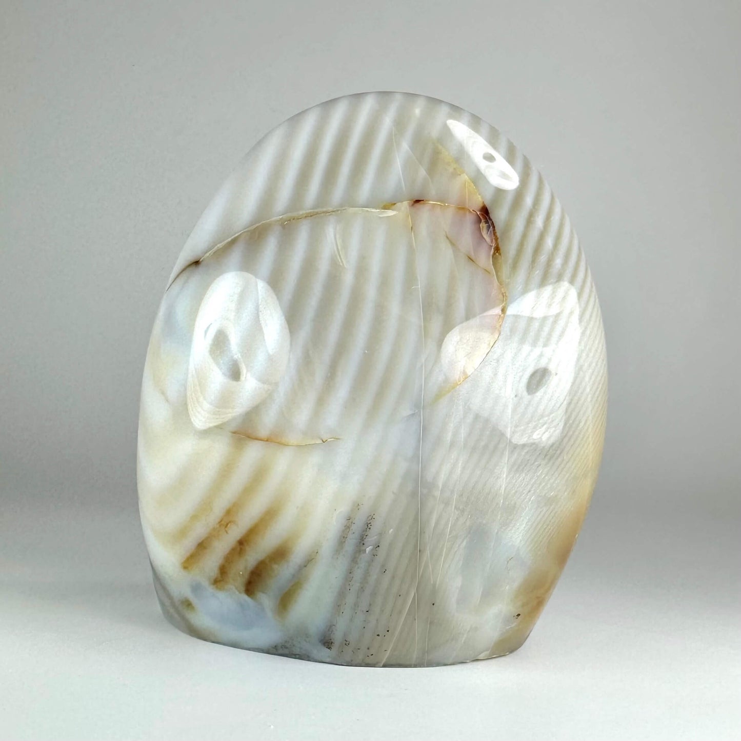 Agat dendrit fri form med lys beige og brunlige striber på en grå baggrund.