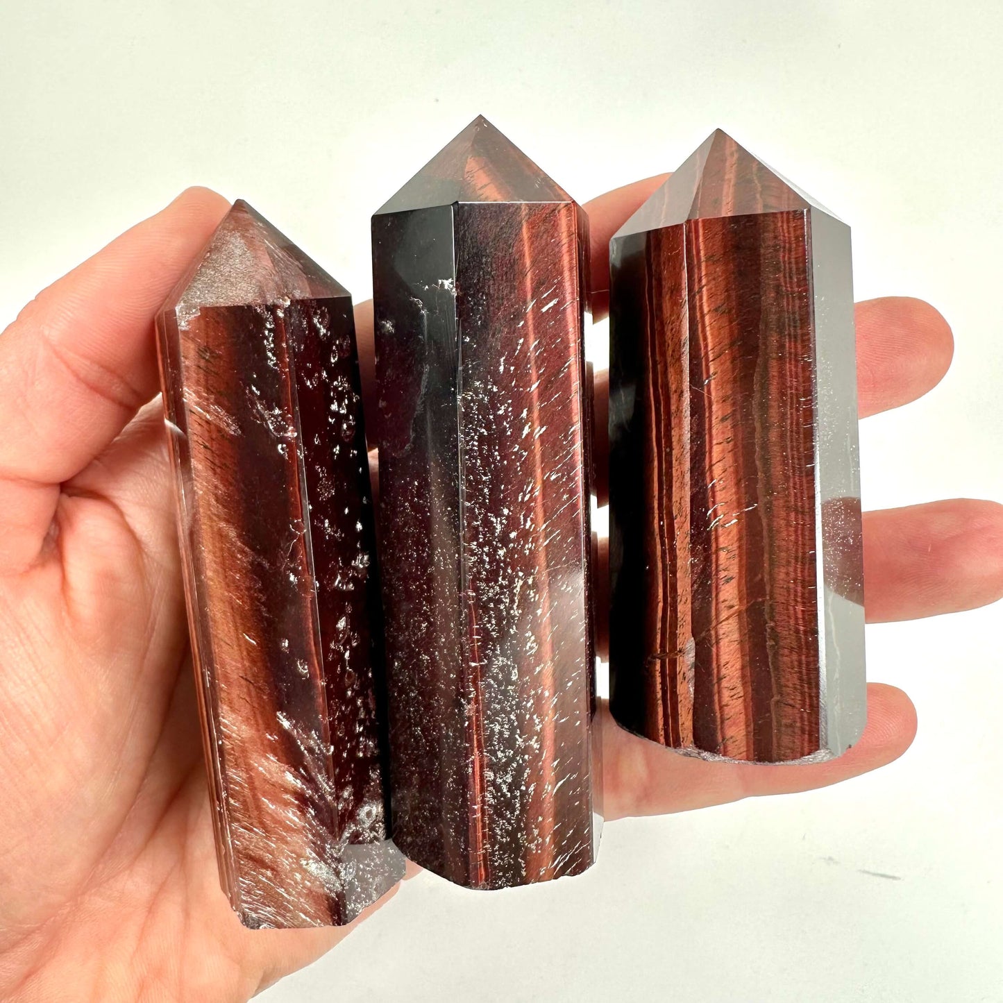 Hånd holder tre Okseøje tårn sten med en brun og rødlig glans på en hvid baggrund.