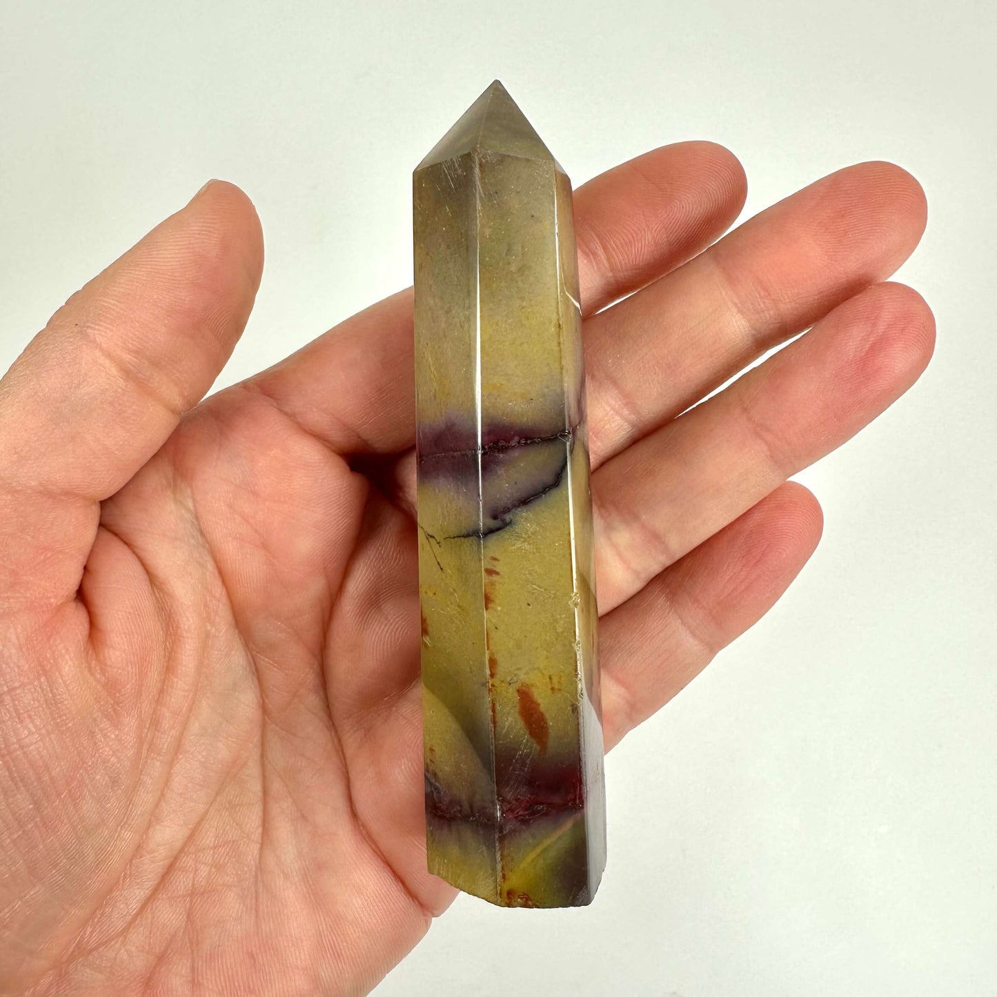 Hånd holder et Mookait tårn med flerfarvede nuancer, inklusive gul og lilla.