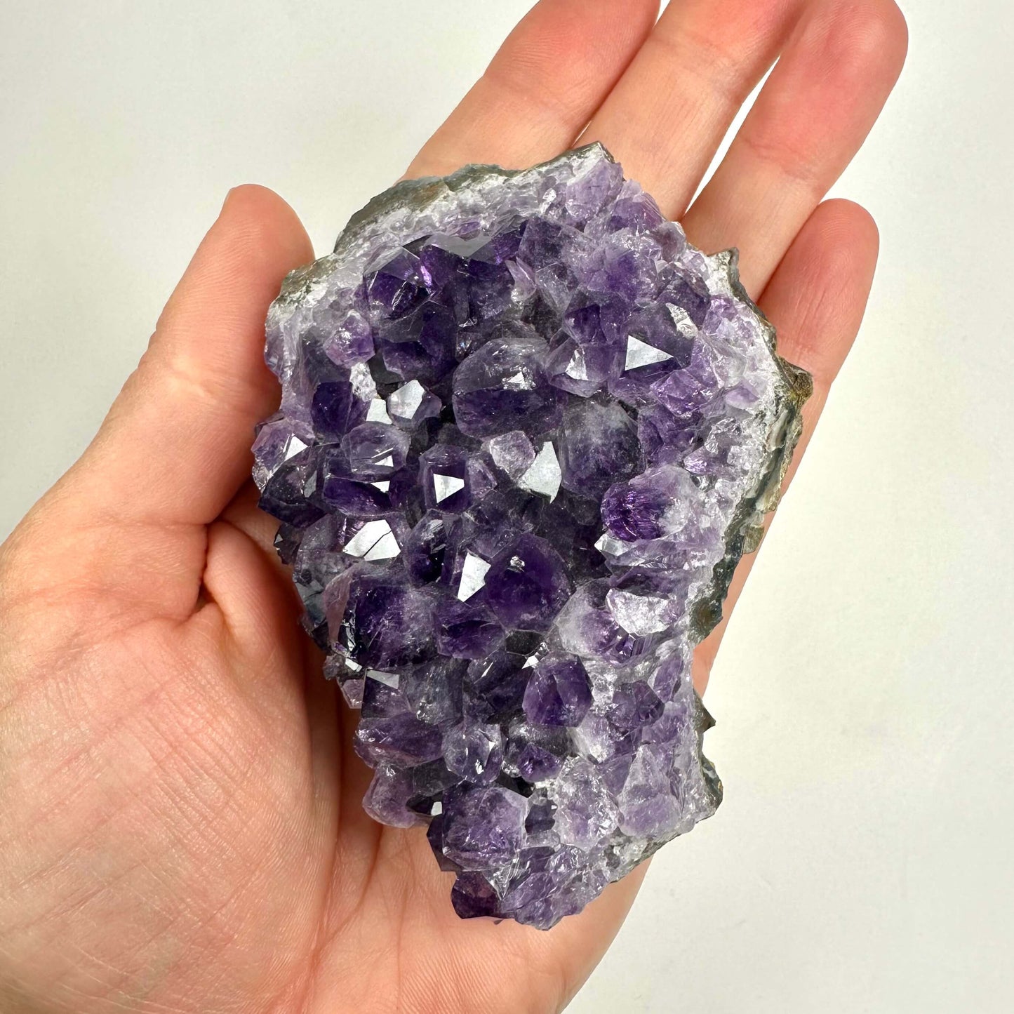 En hånd holder en Ametyst klynge med lilla krystaller mod en lys baggrund.