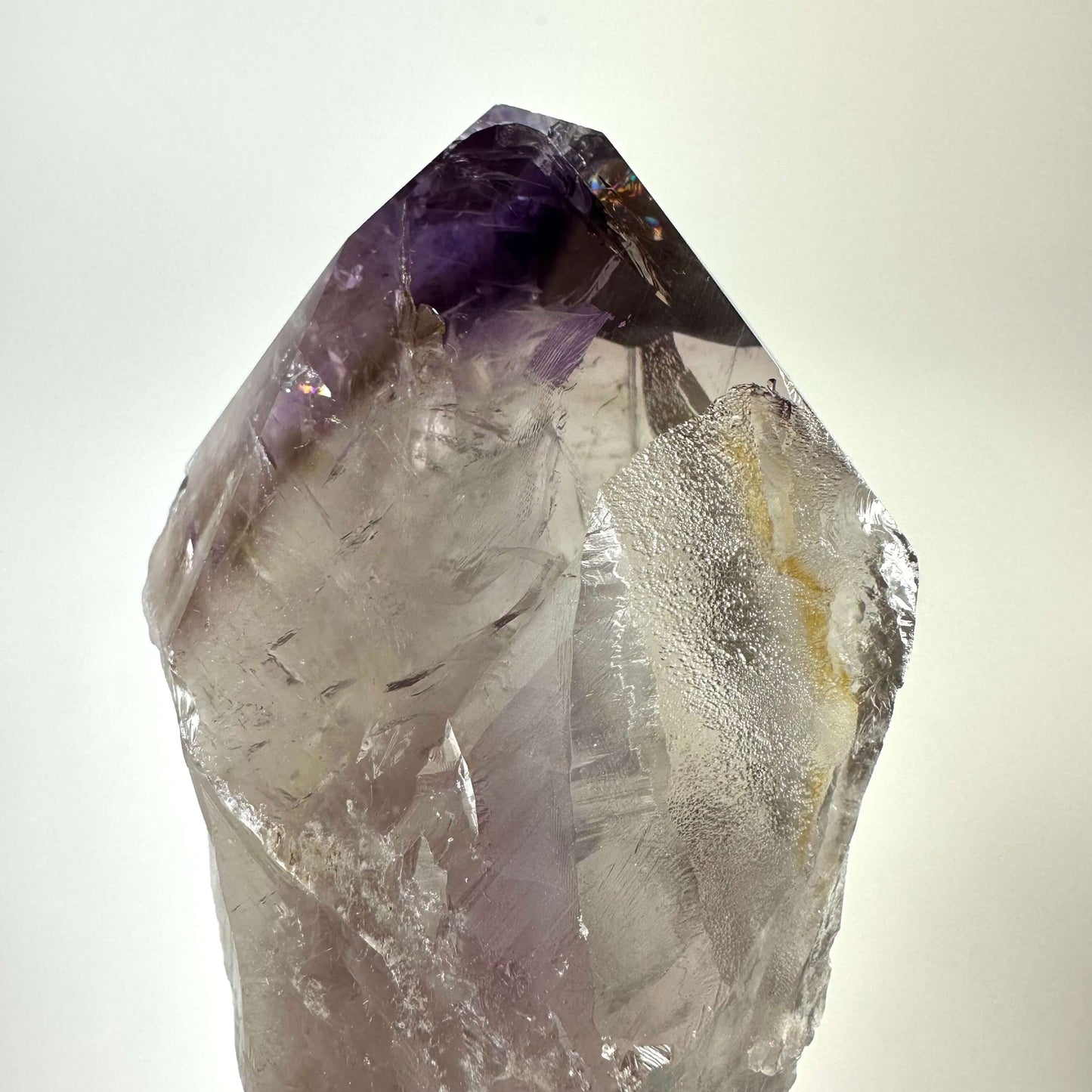 Ametyst scepter med glatte og ru overflader, viser en lilla nuance på toppen mod en hvid baggrund.