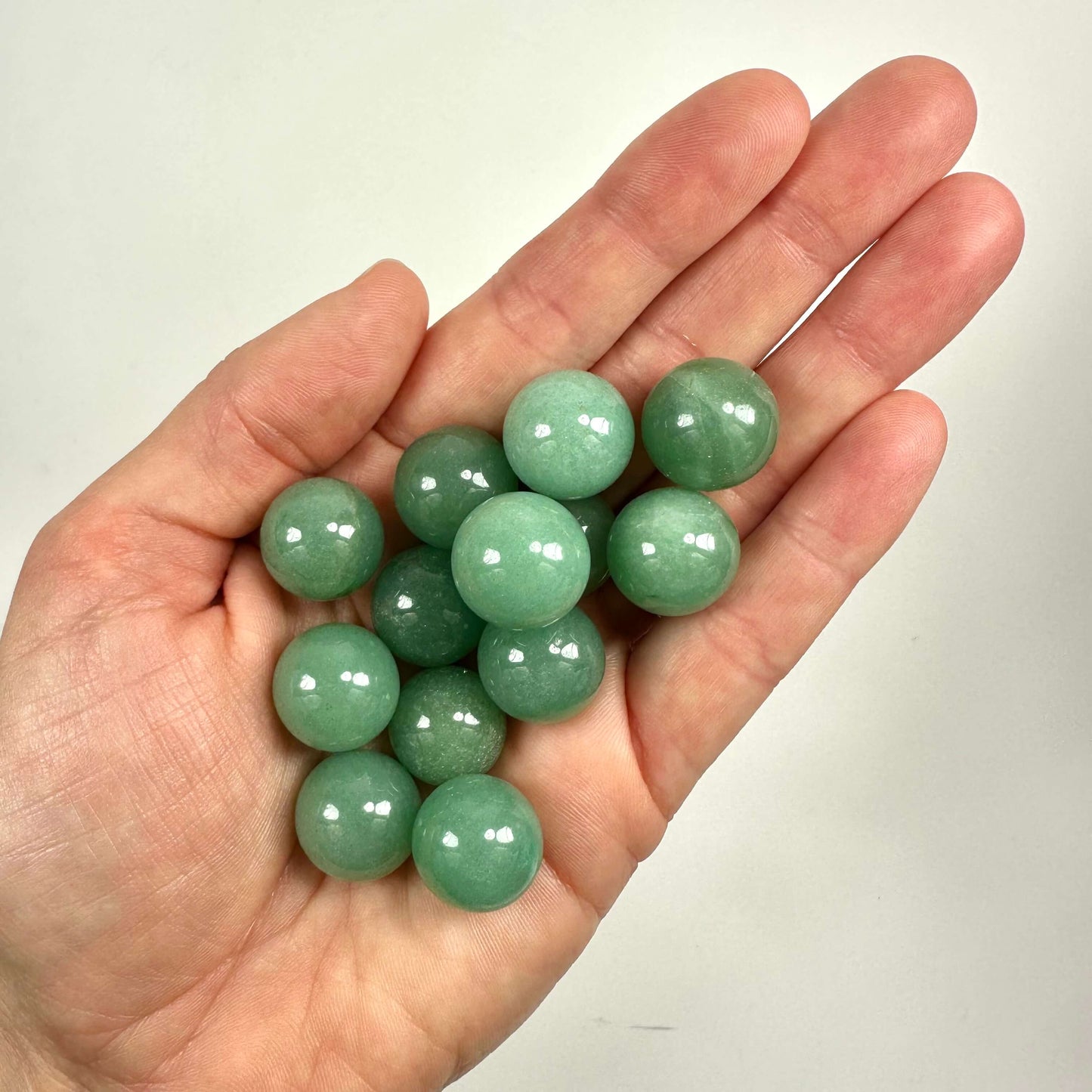Håndfuld Grøn Aventurin kugler, der glitrer i håndfladen på en neutral baggrund.