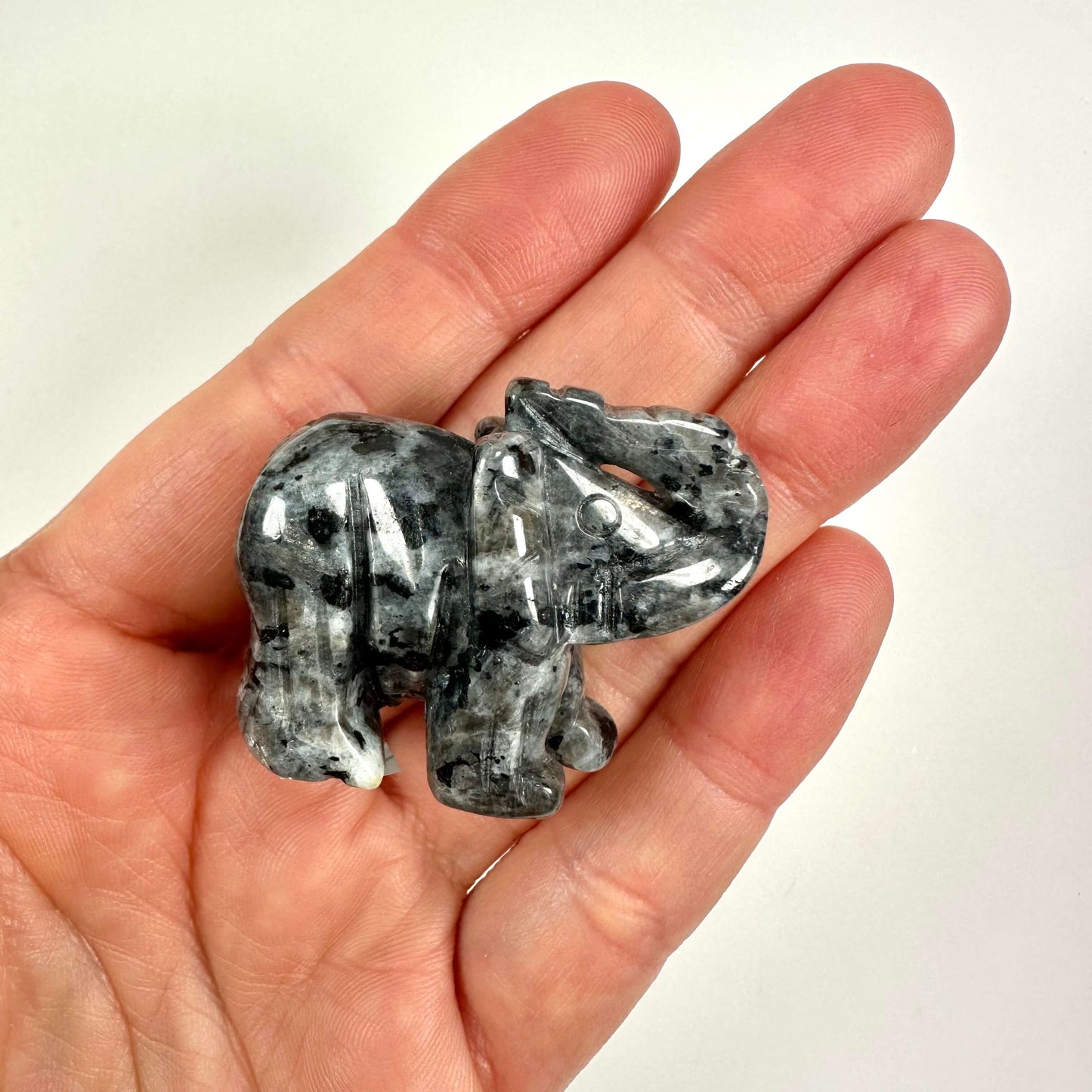 Larvikit elefantfigur placeret i en hånd, viser stenens unikke skinnende overflade og mønster.