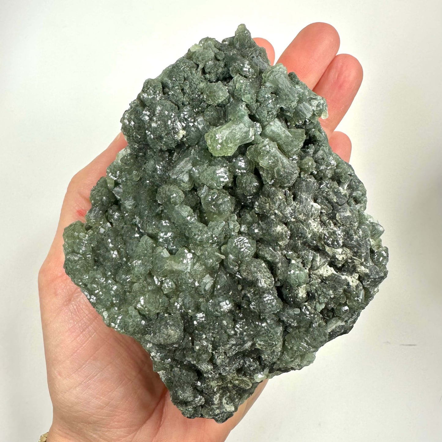 En hånd holder en stor Prehnit klynge med grønne, krystallinske formationer.