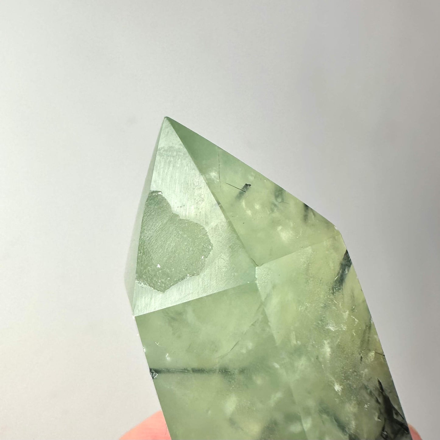 Prehnit tårn med lysegrønne nuancer og delikate indre inklusioner mod en lys baggrund.