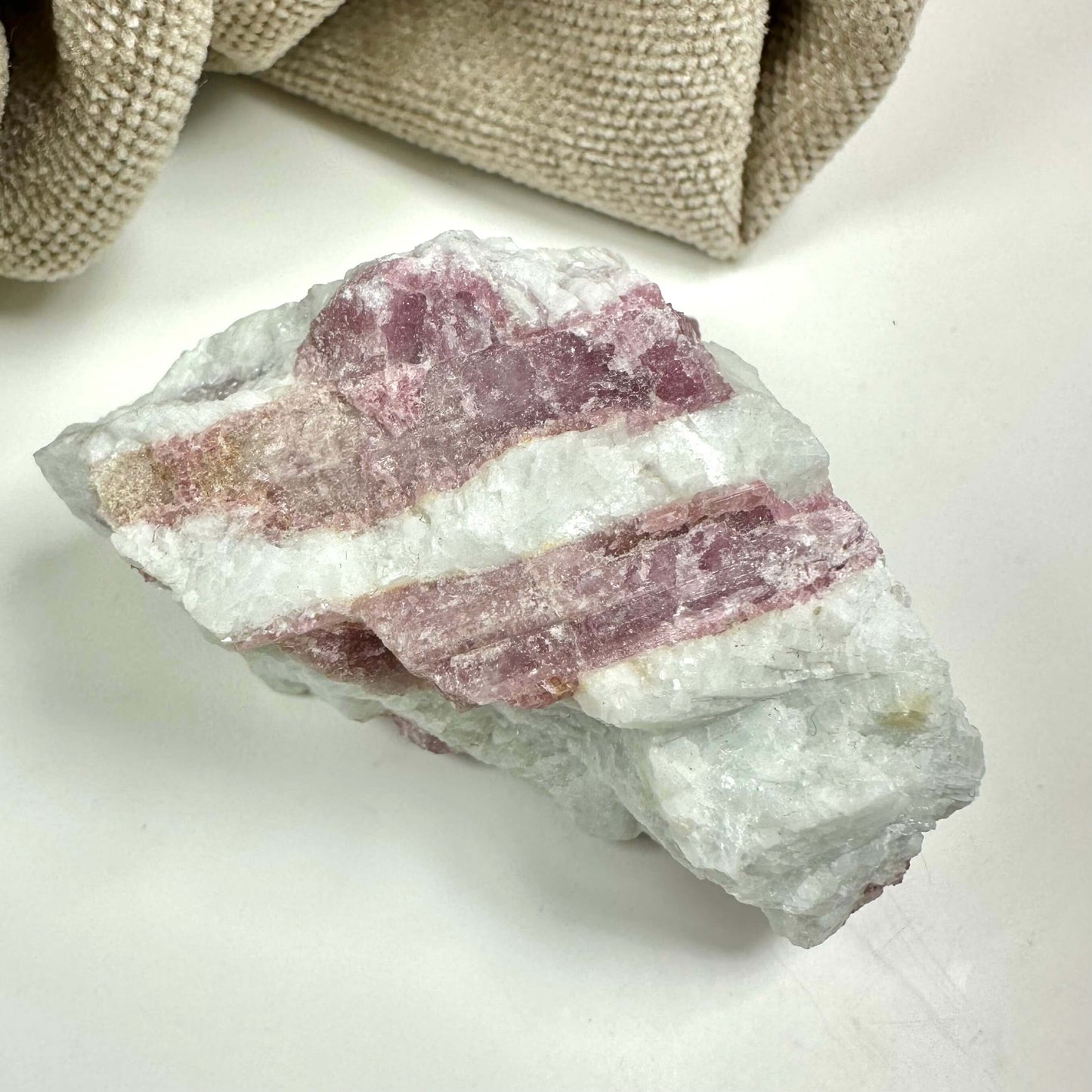 Rå Rubellit kvarts med hvide og lyserøde striber på en lys baggrund.