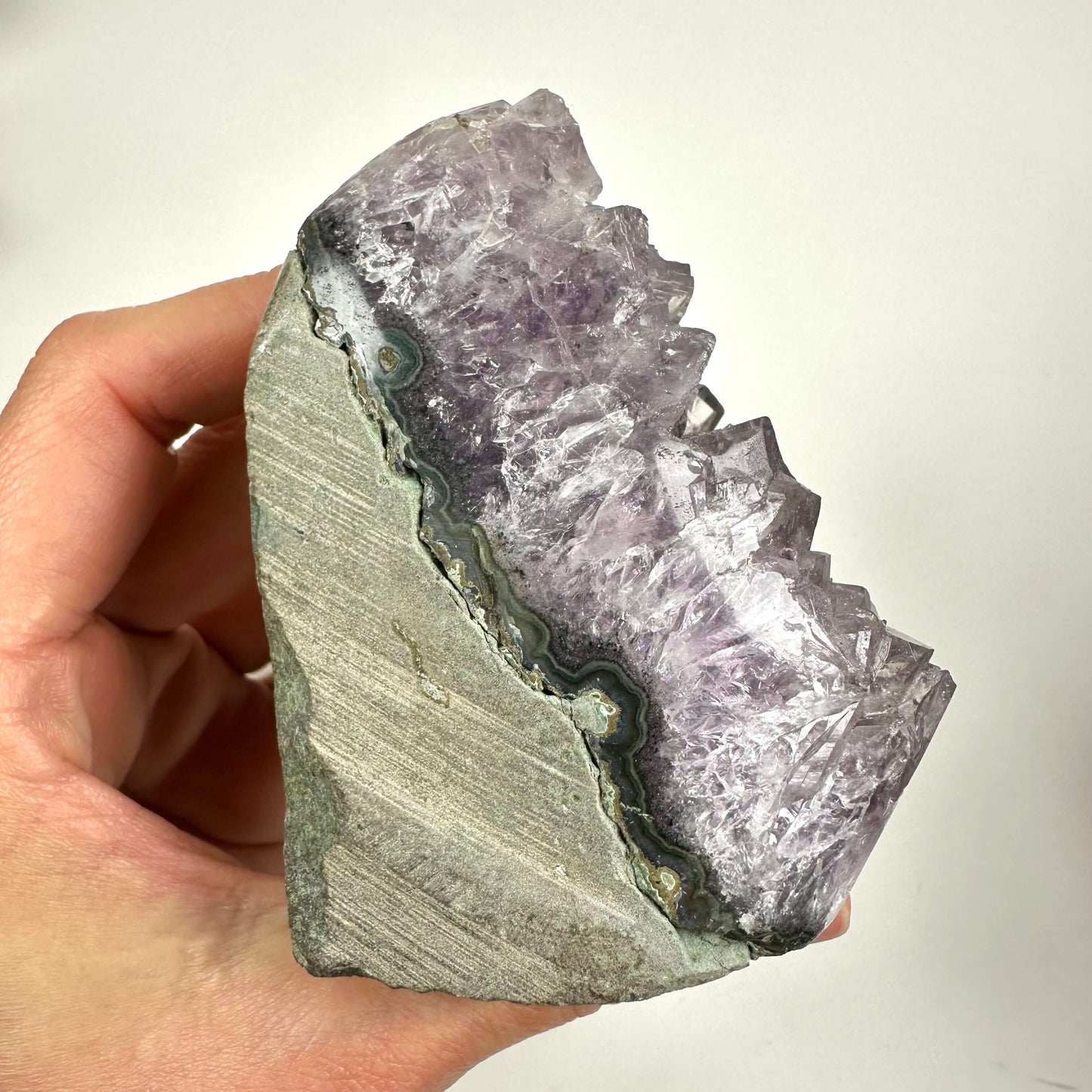 En hånd holder en ametystkrystal i fri form med synlige lilla nuancer og rå kanter.