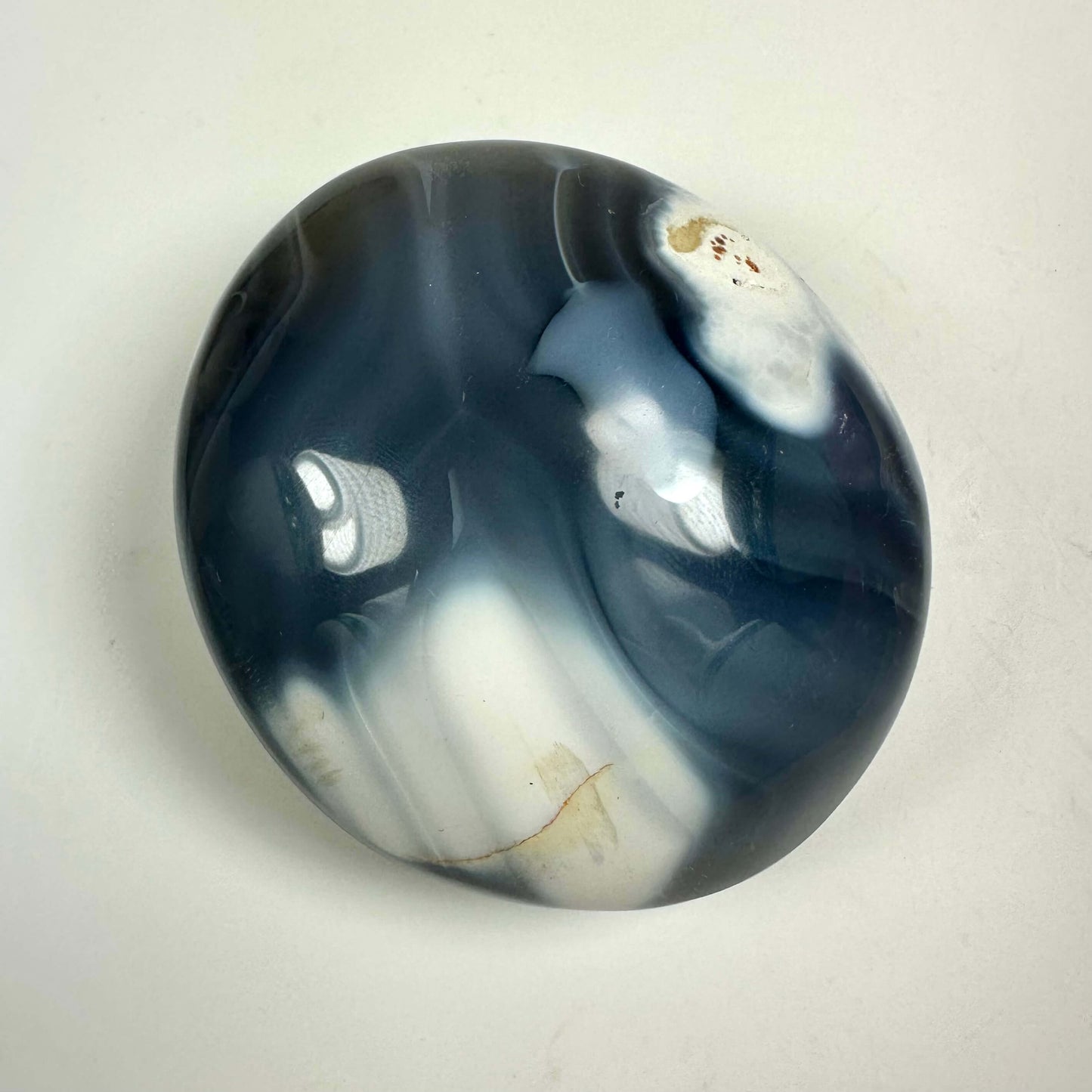 Orca agat palmstone med glatte, mørke og lyse mønstre på en lys overflade.