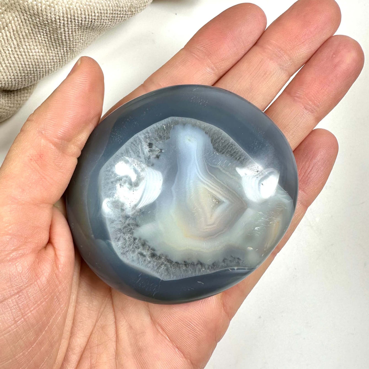 Hånd holder en Orca agat palmesten med glatte, polerede overflader og hvid-grålige nuancer.