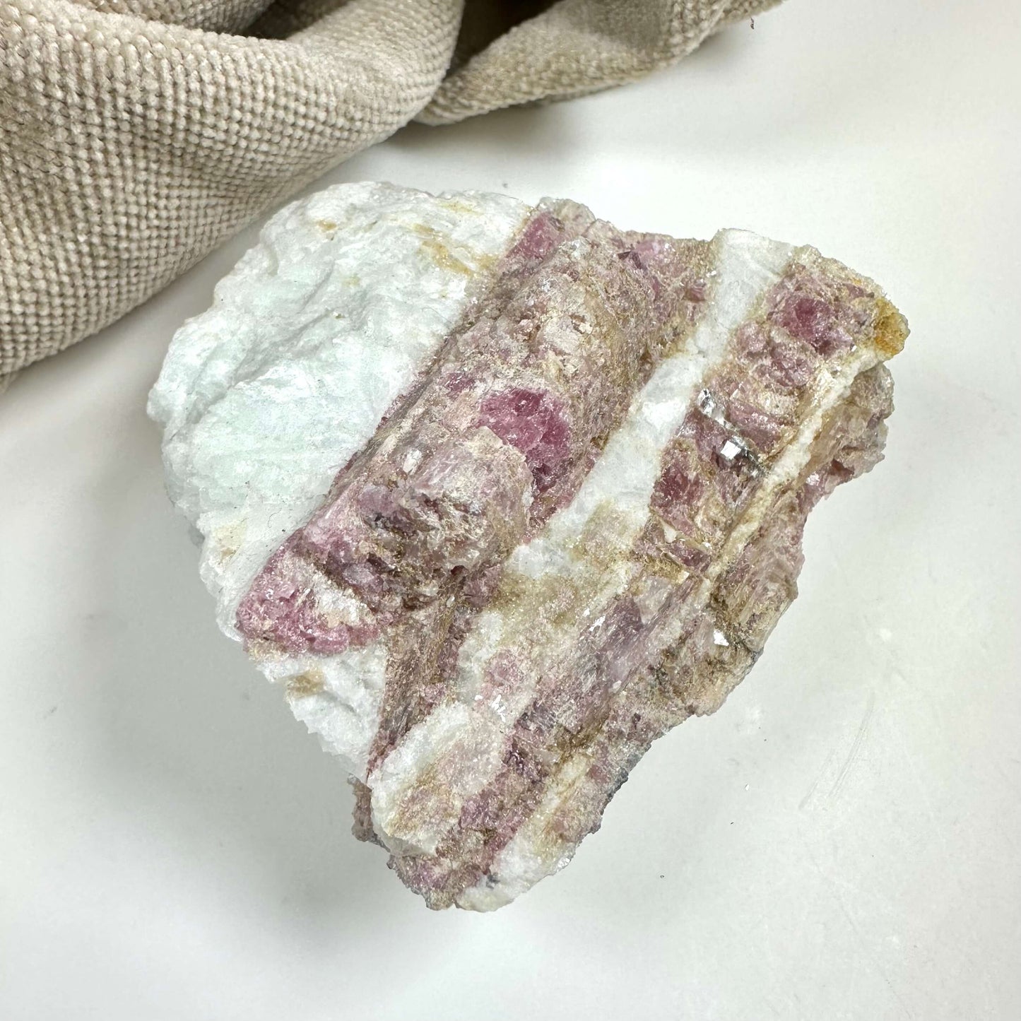 Rubellit kvarts rå med pink nuancer på hvid baggrund, ved siden af beige stof.
