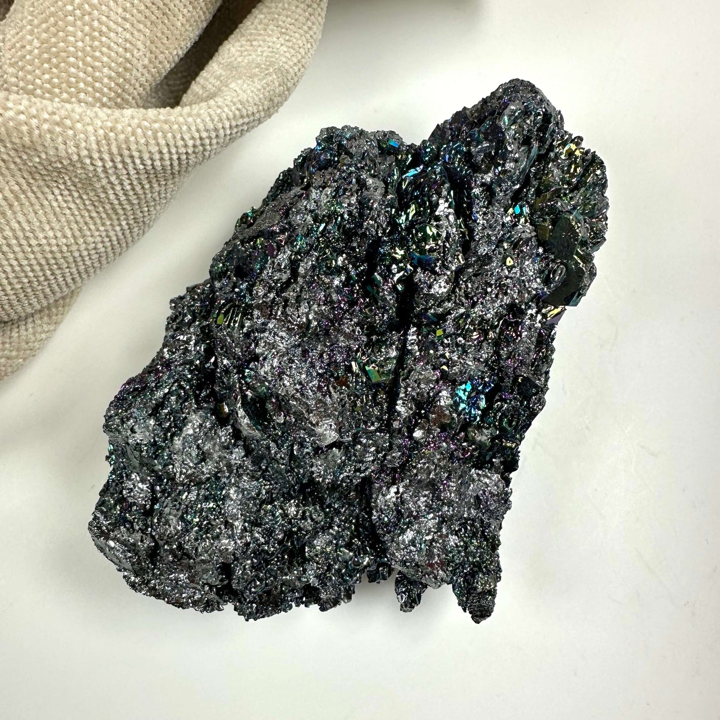 Heksesten klynge med flerfarvede, skinnende krystaller på en lys baggrund ved siden af en beige klud.