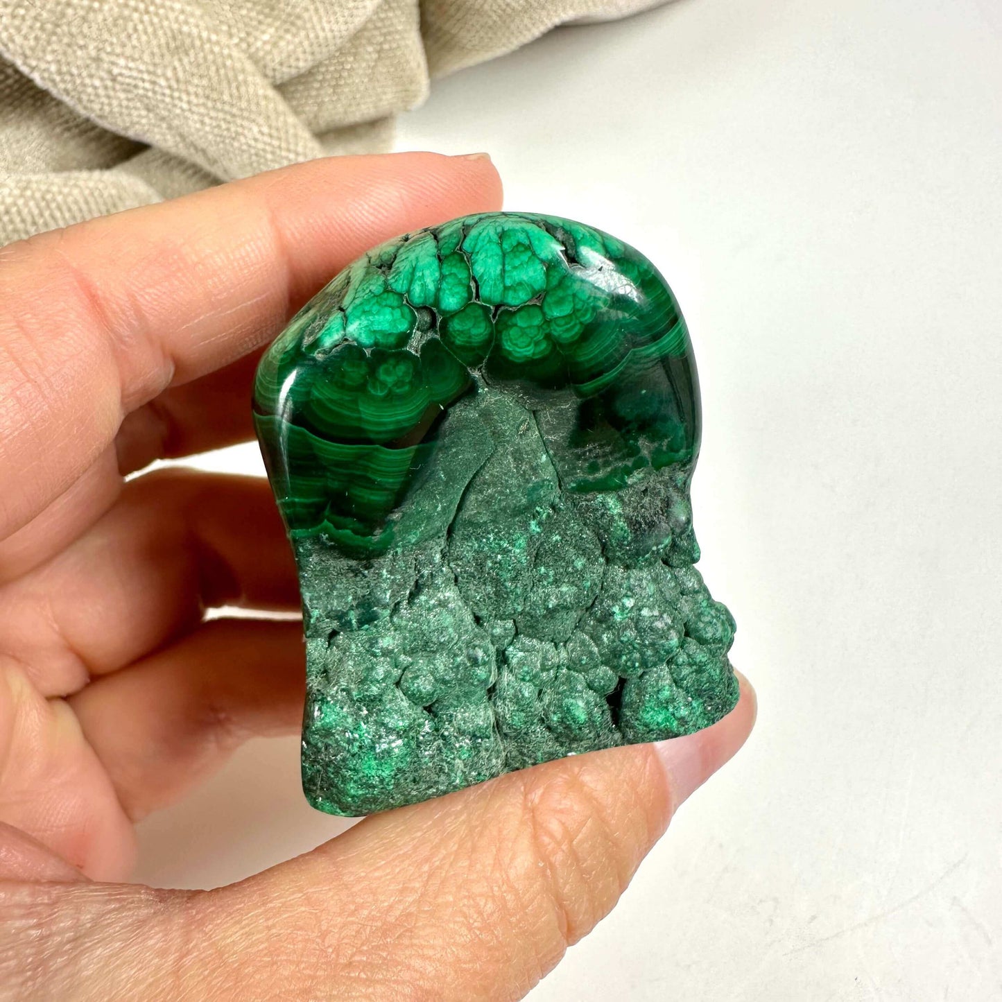 Hånd holder en poleret malakit, viser dens karakteristiske grønne bånd og mønstre.
