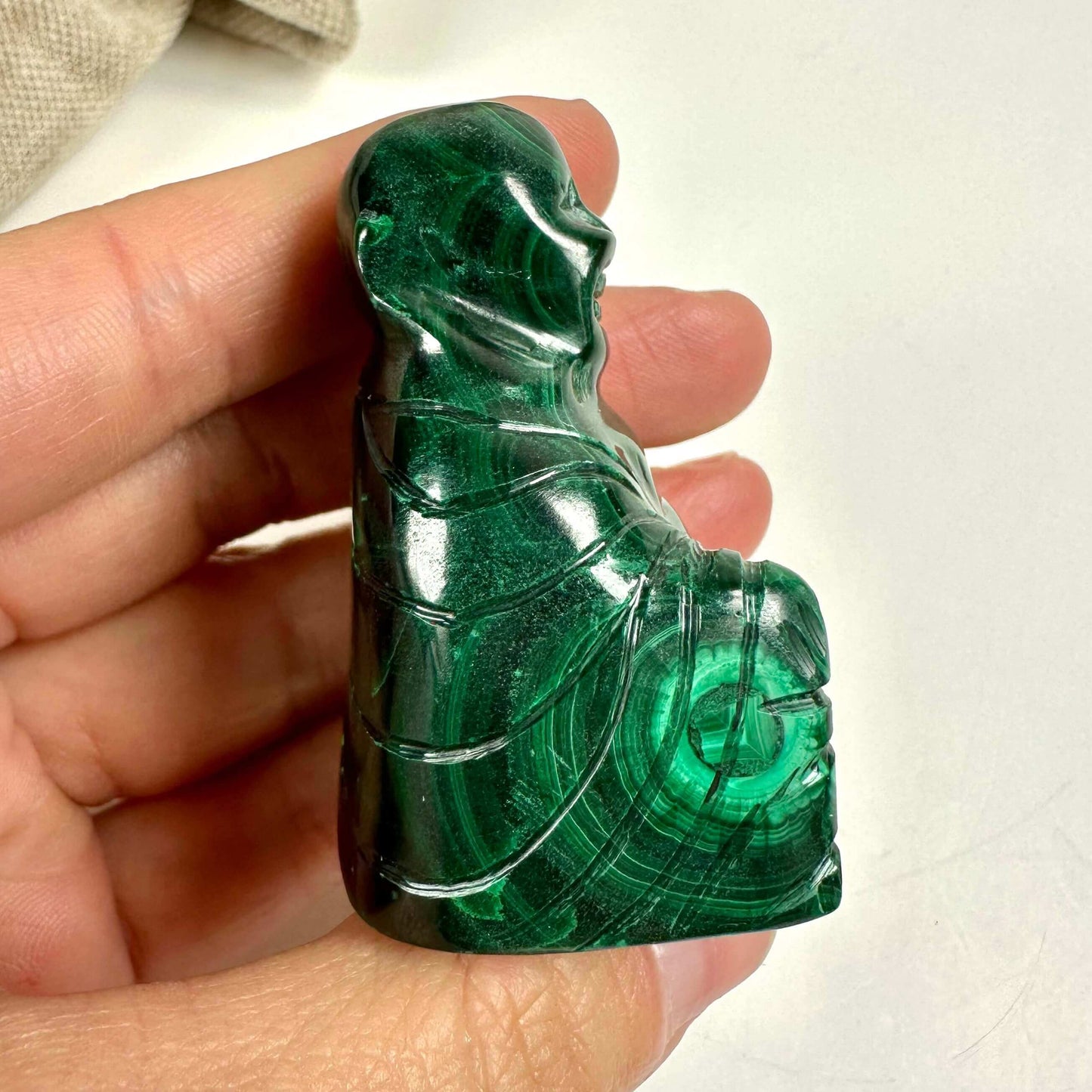 Hånd, der holder en Malakit Buddha-figur, detaljeret udskåret i smuk grønt malakit.