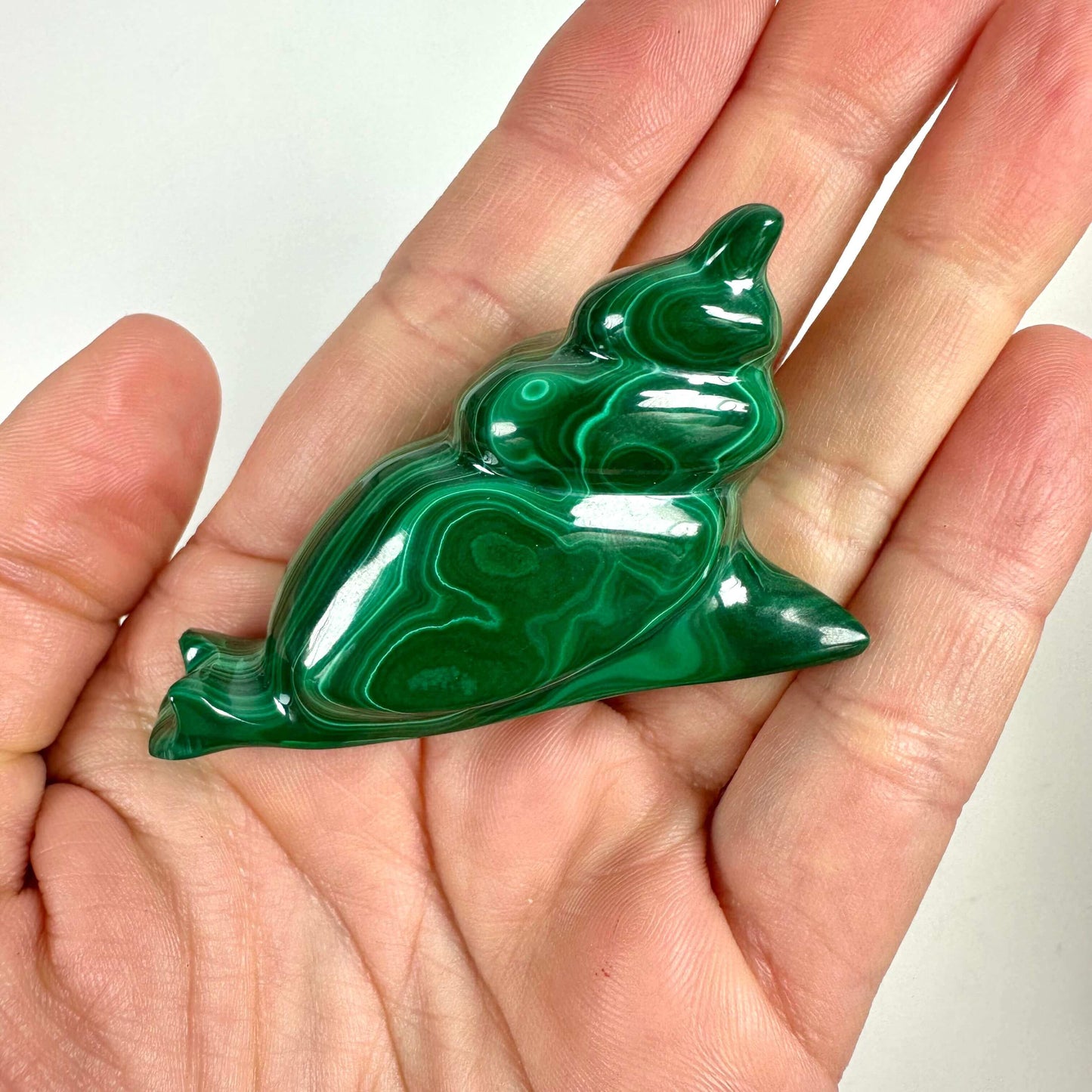 Hånd holder en skulptur af en malakit snegl med grønne mønstre.