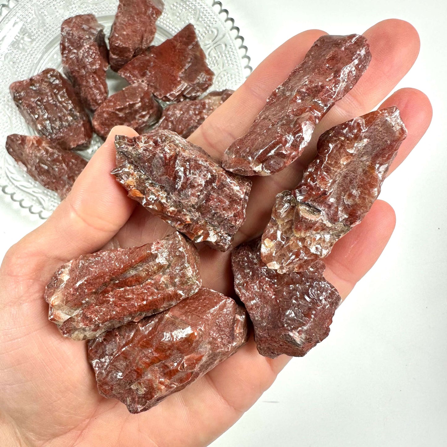 En håndfuld rå rød calcitkrystaller ligger spredt i en åben håndflade.