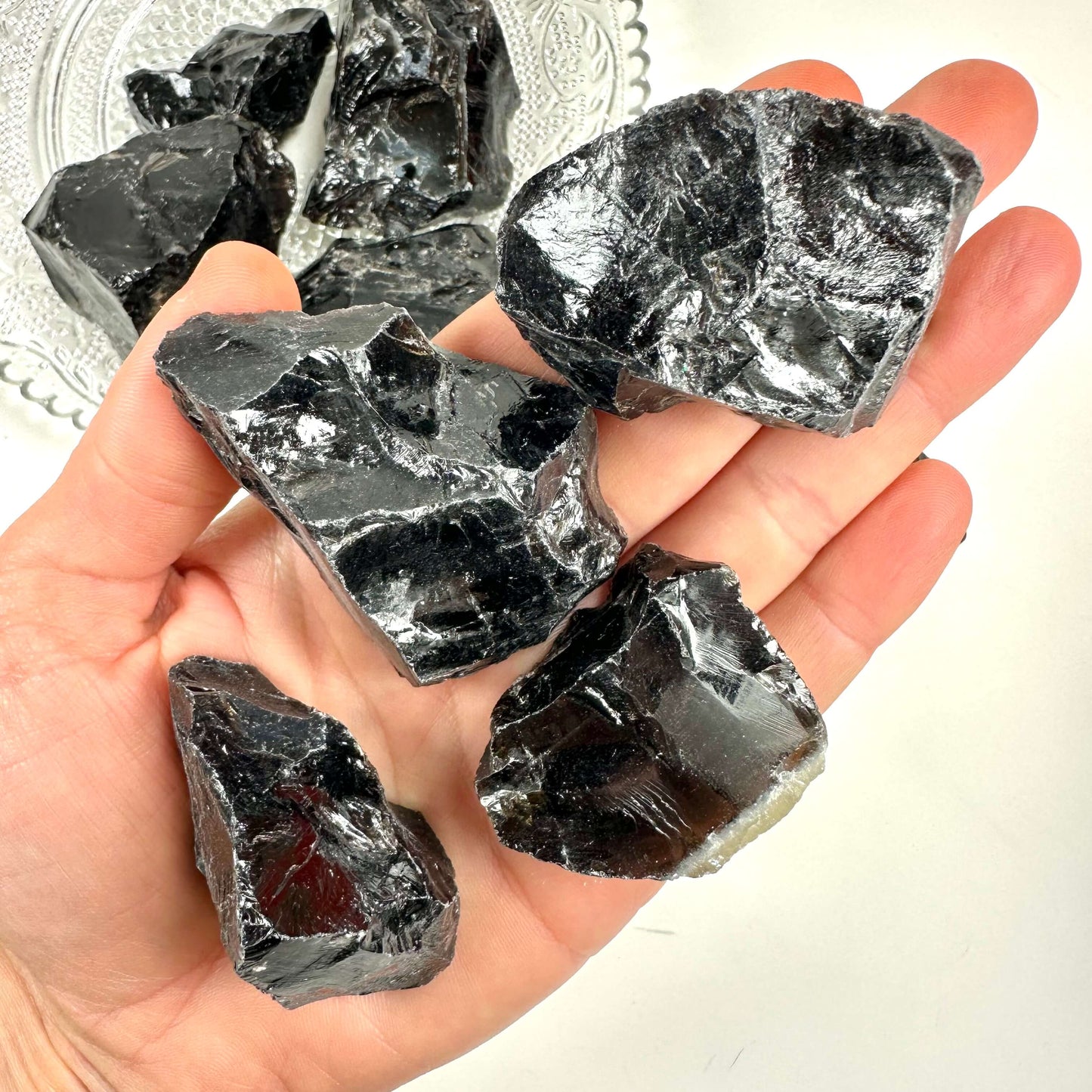 Hånd holder flere rå morion, sorte og skinnende krystaller, over en dekoreret glasplade.