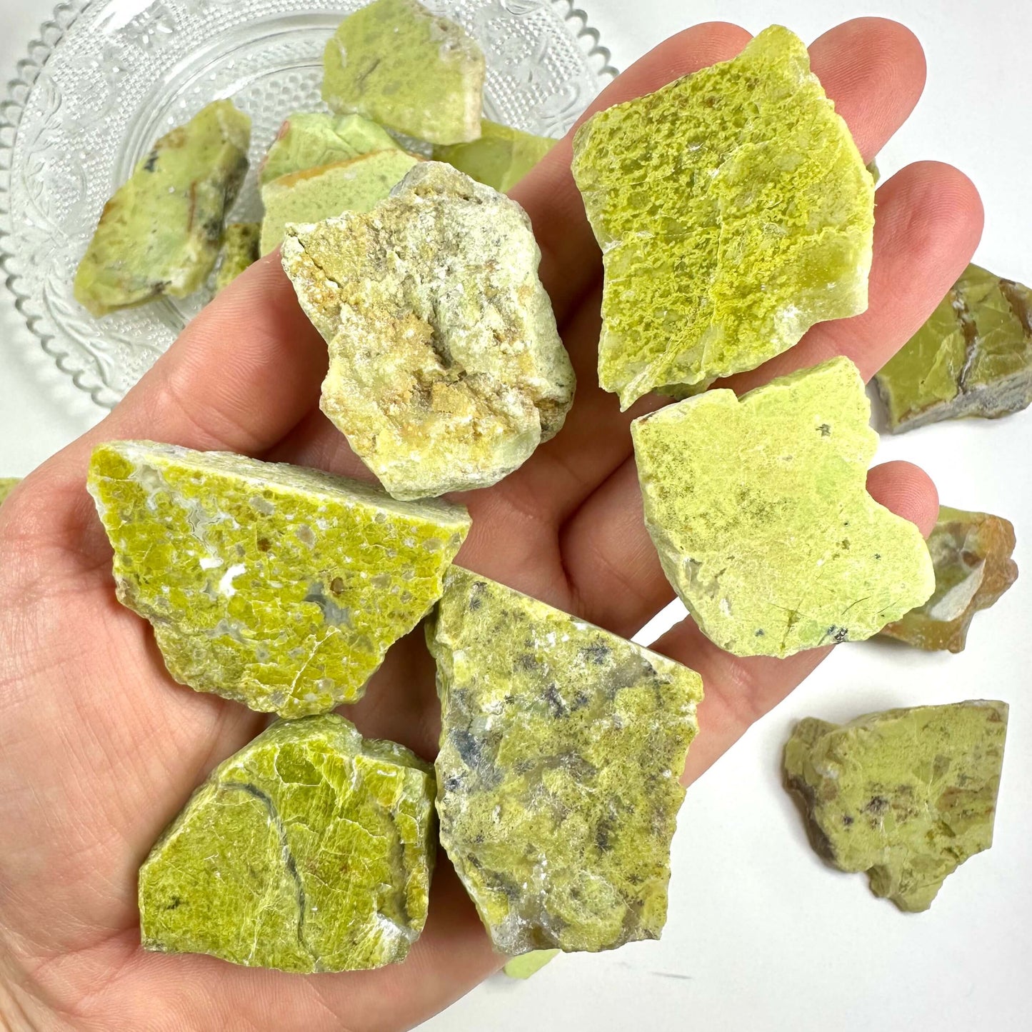 Hånden holder flere grønne mineralsten på en tallerken.