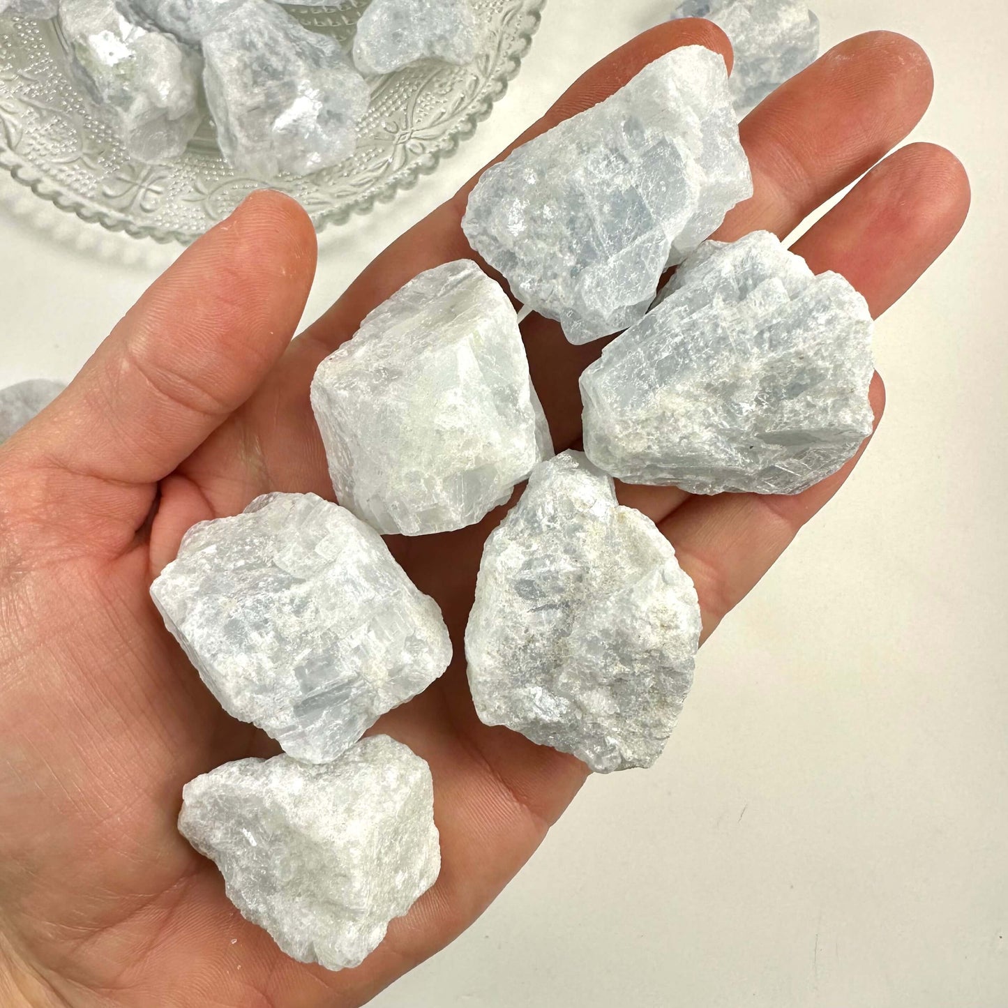 Hånd med flere stykker blå calcit rå på en lys baggrund.