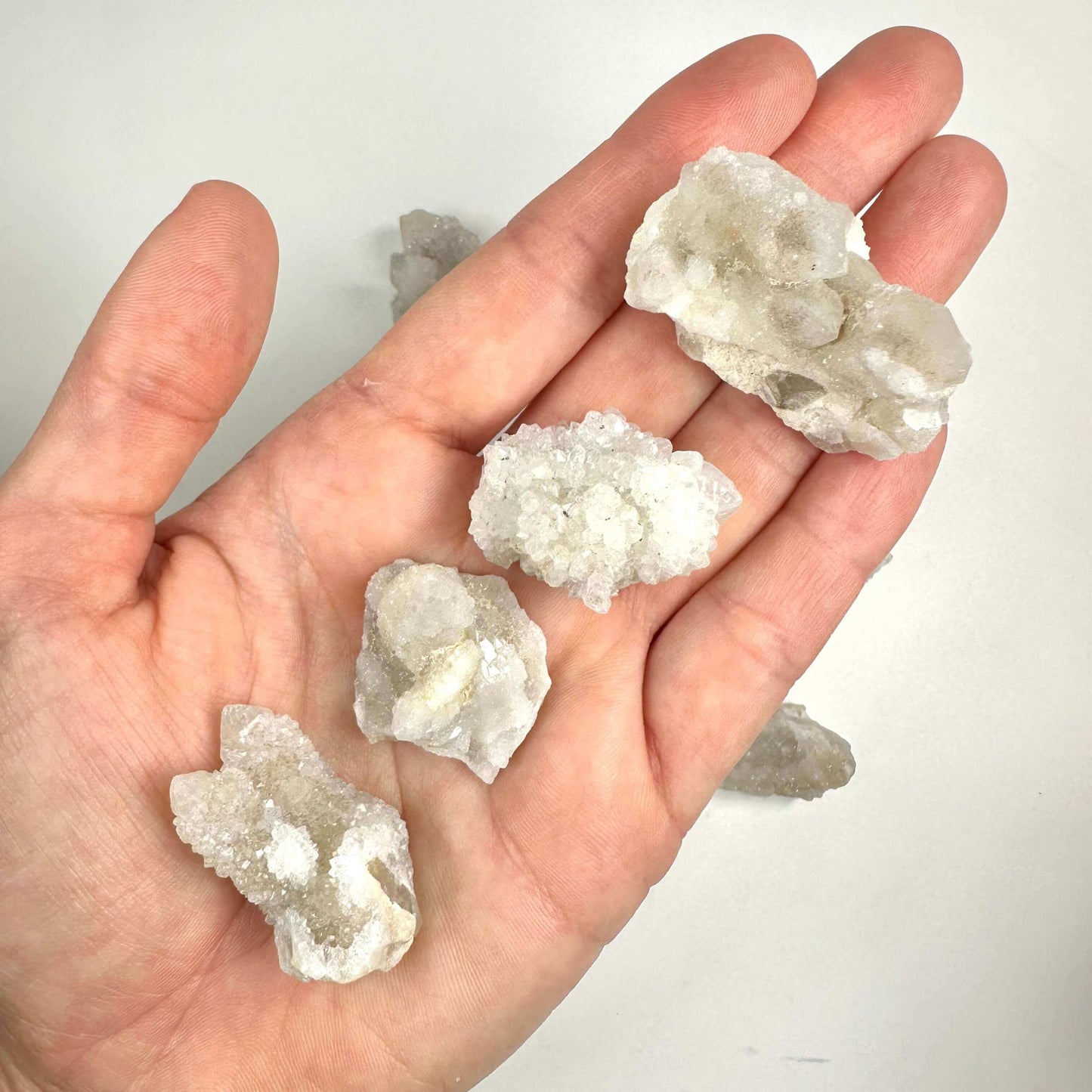 En hånd holder fire stykker spiritkvarts klynge mod en lys baggrund.