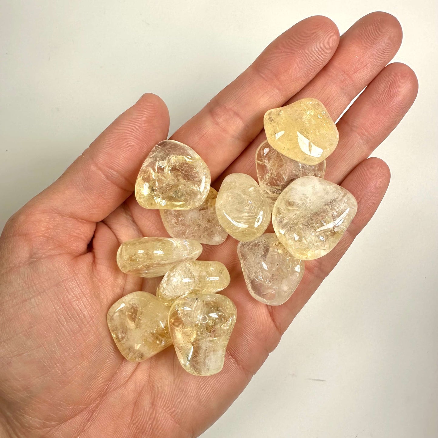 Håndfuld Brændt Citrin krystaller i en hånd på en lys baggrund.