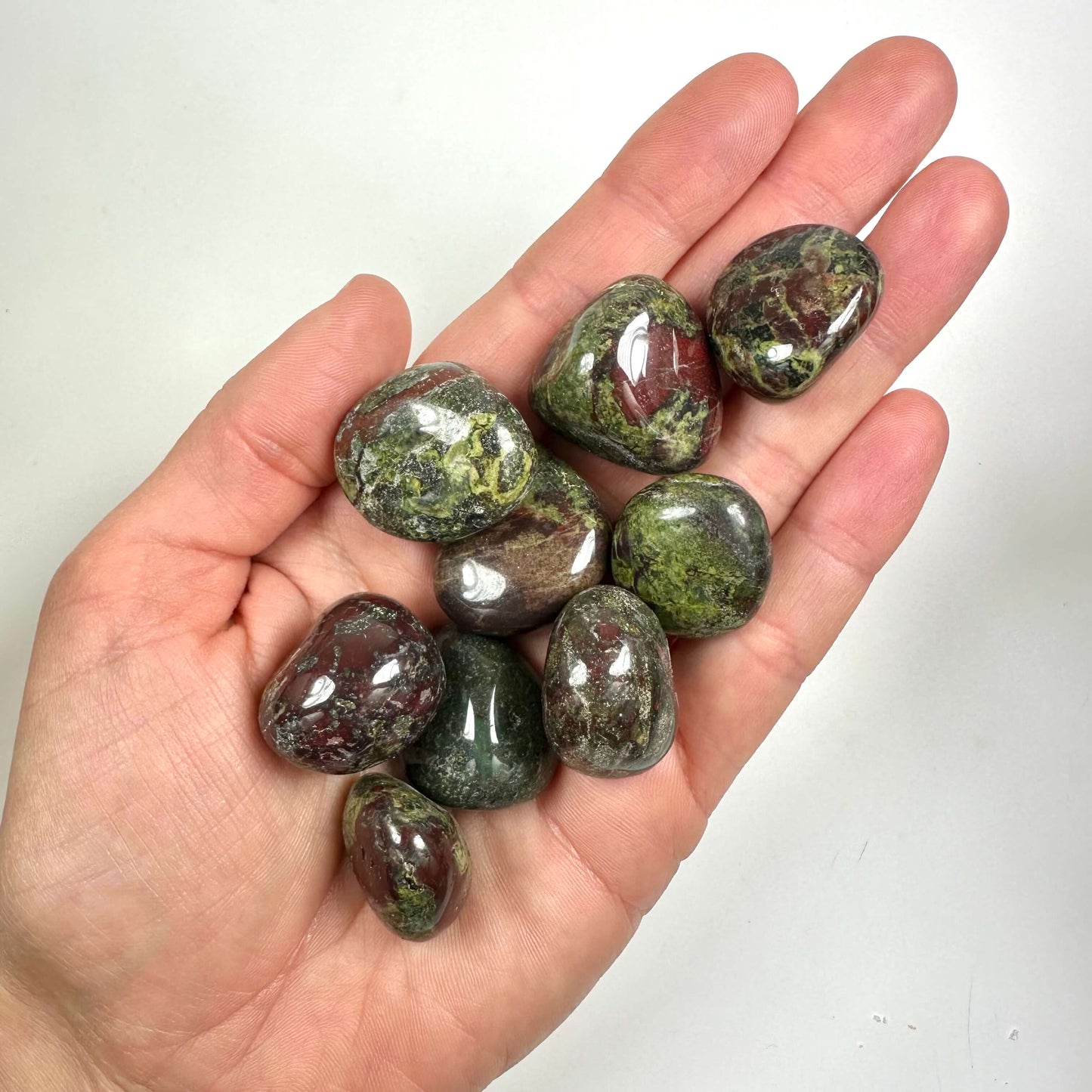 En hånd holder flere skinnende Drageblod lommesten i røde og grønne nuancer.