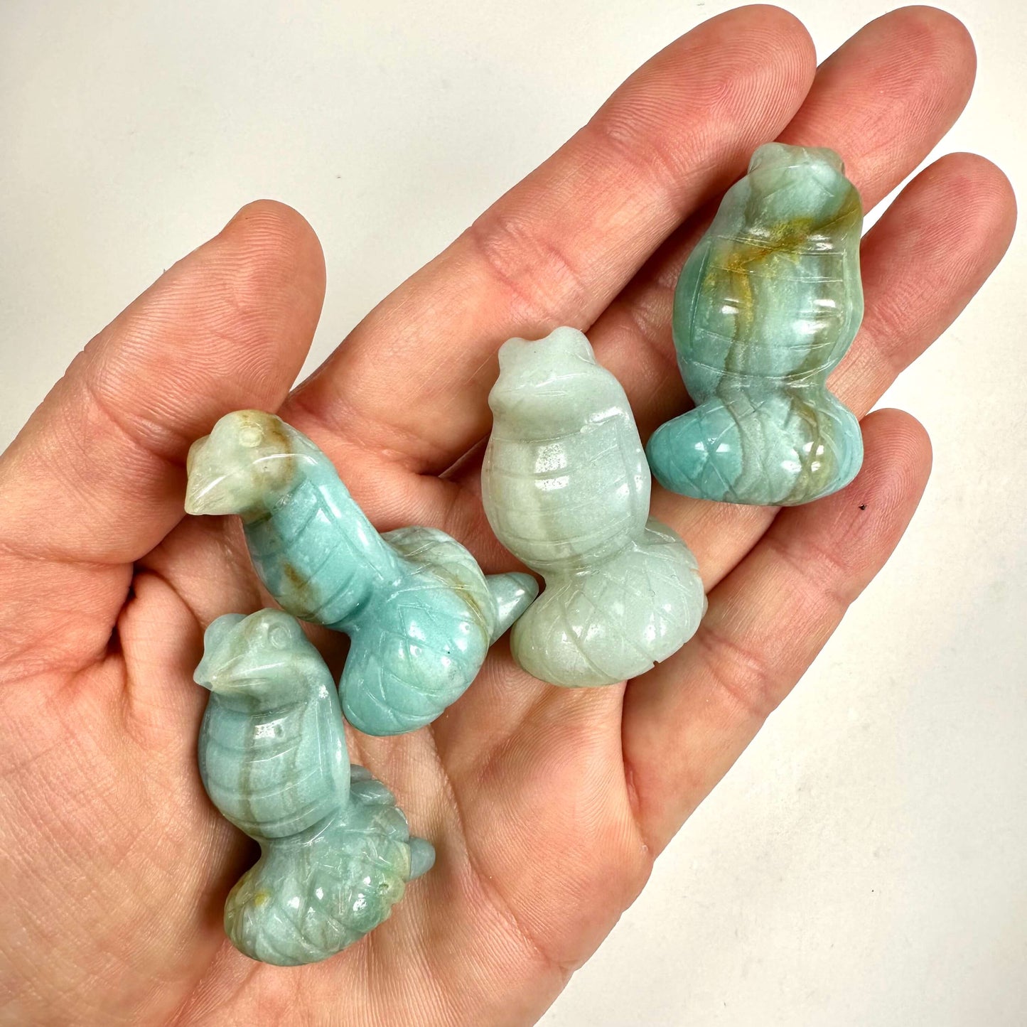 Hånd holder fire skulpturer af amazonit slangeform, i lyseblå og hvidlige nuancer.
