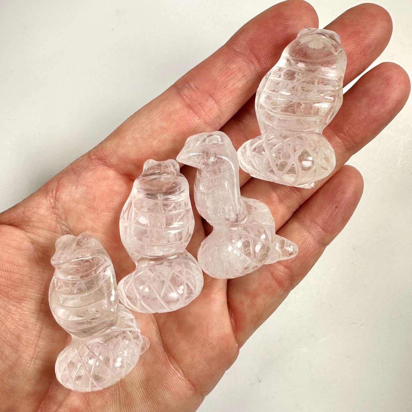 Hånd med fire små bjergkrystal slangefigurer, udskåret med fine detaljer.