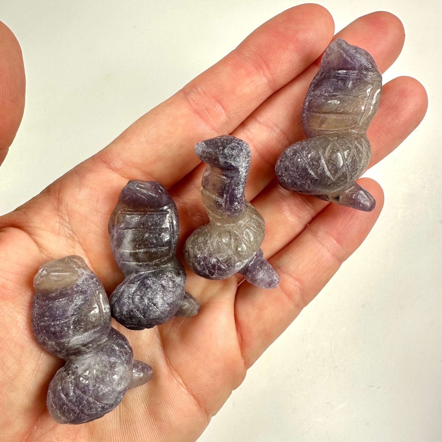 Hånd, der holder fire udskårne lepidolit slanger i lilla nuancer.