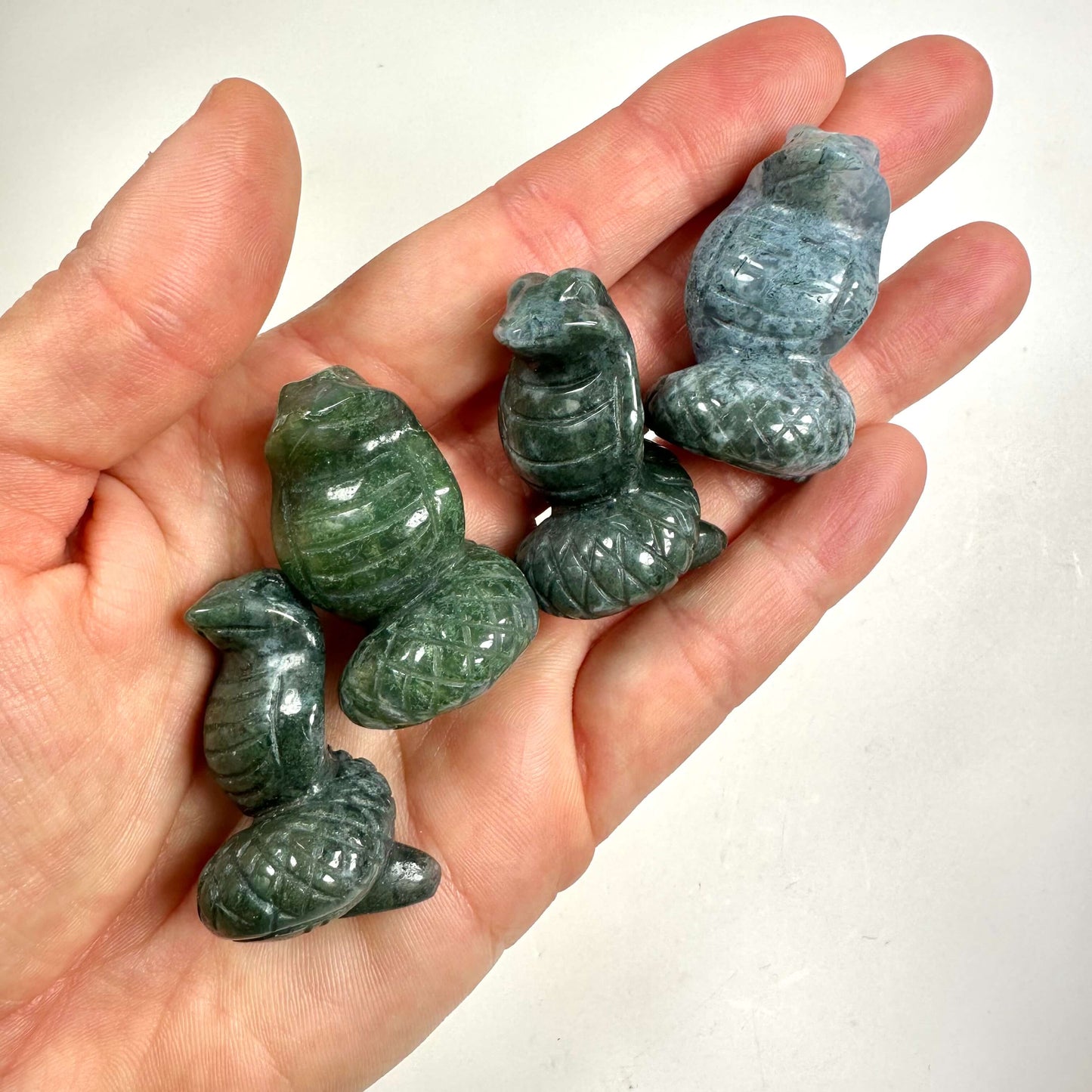 Hånd holder flere små figurer udskåret i Mos Agat, formet som slanger.