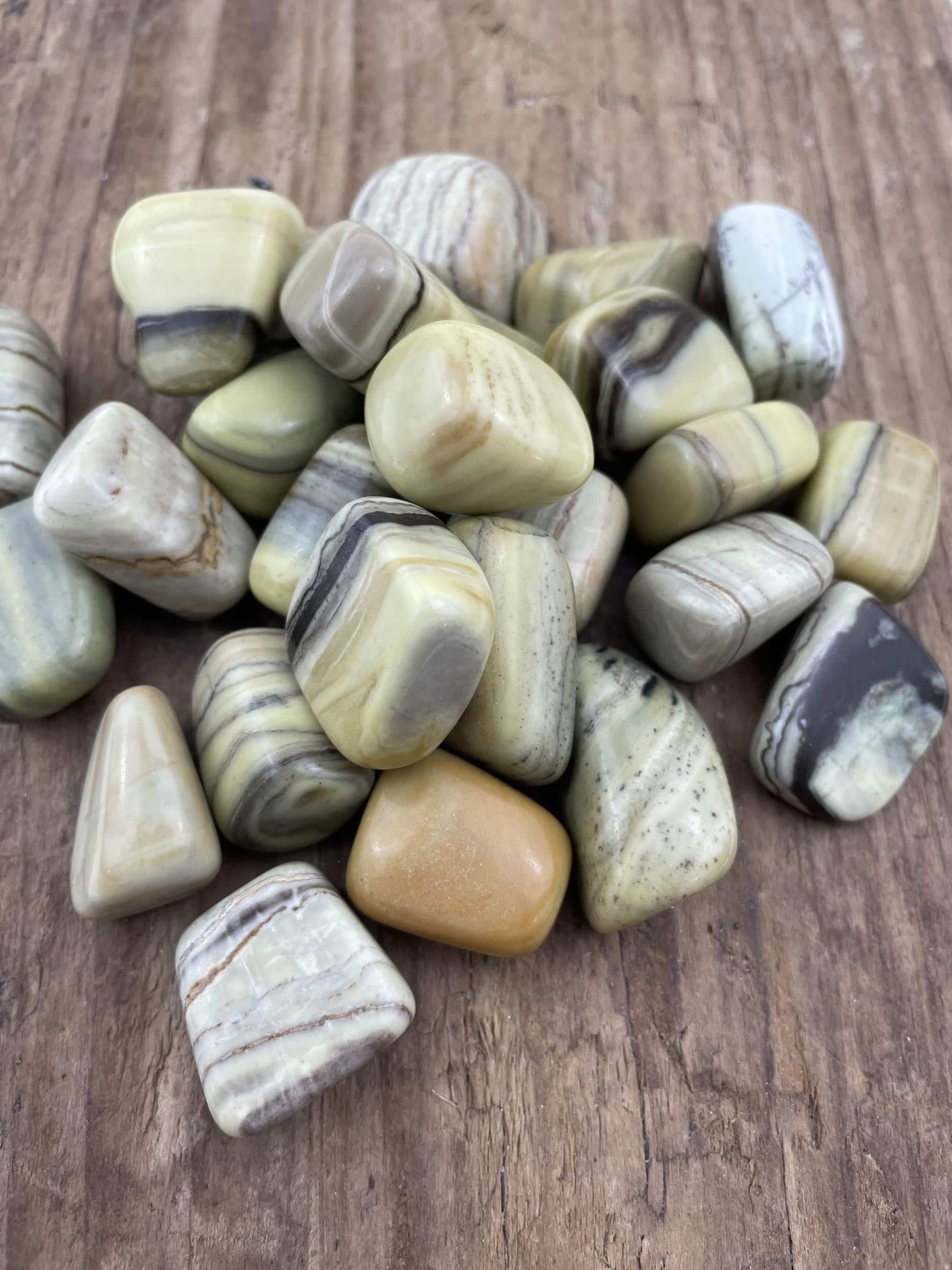 Jade smør lommesten i nuancer af grøn og beige ligger spredt på en træoverflade.