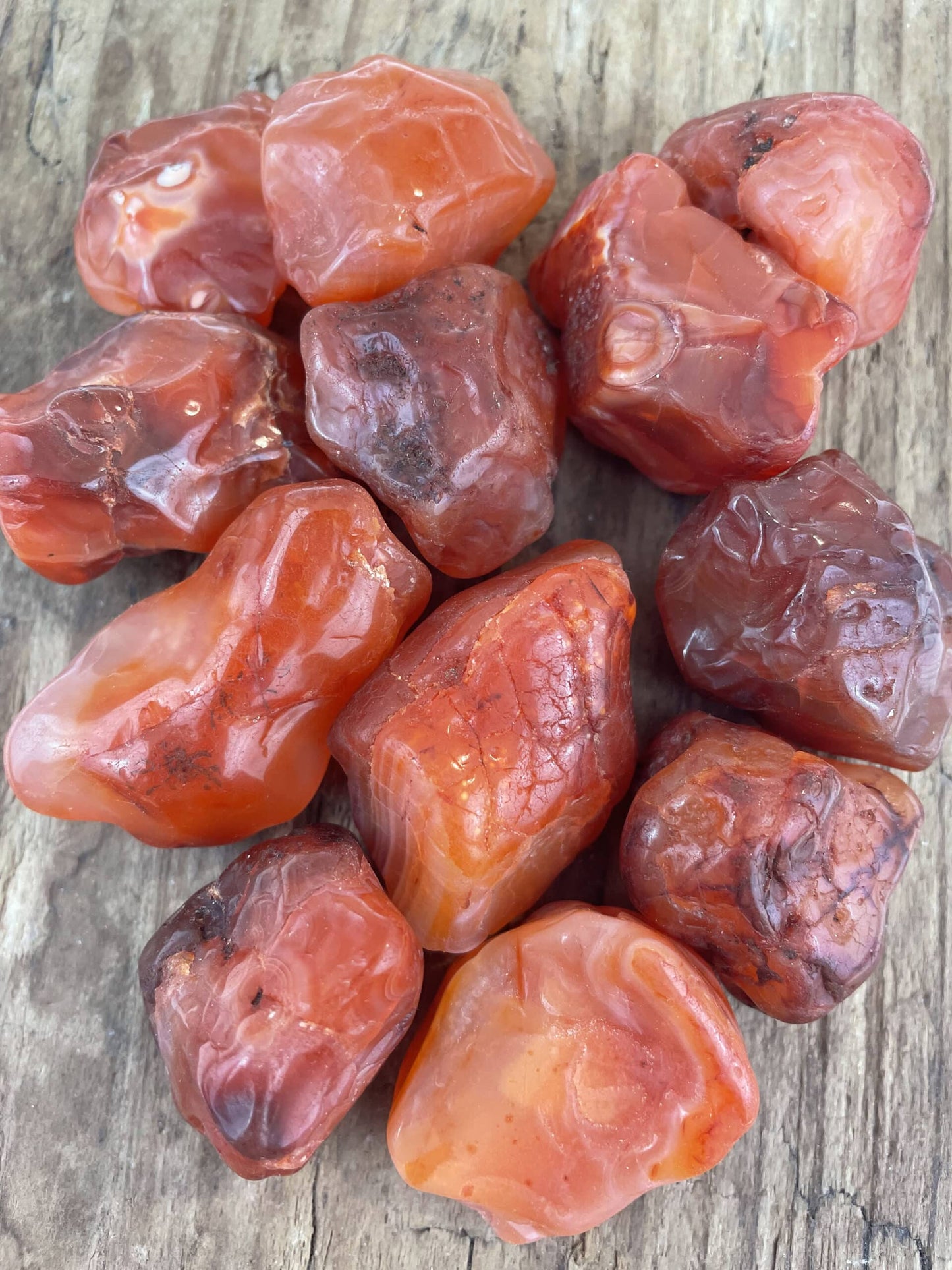 Rå karneolsten i forskellige nuancer af orange og rød ligger på en træoverflade.