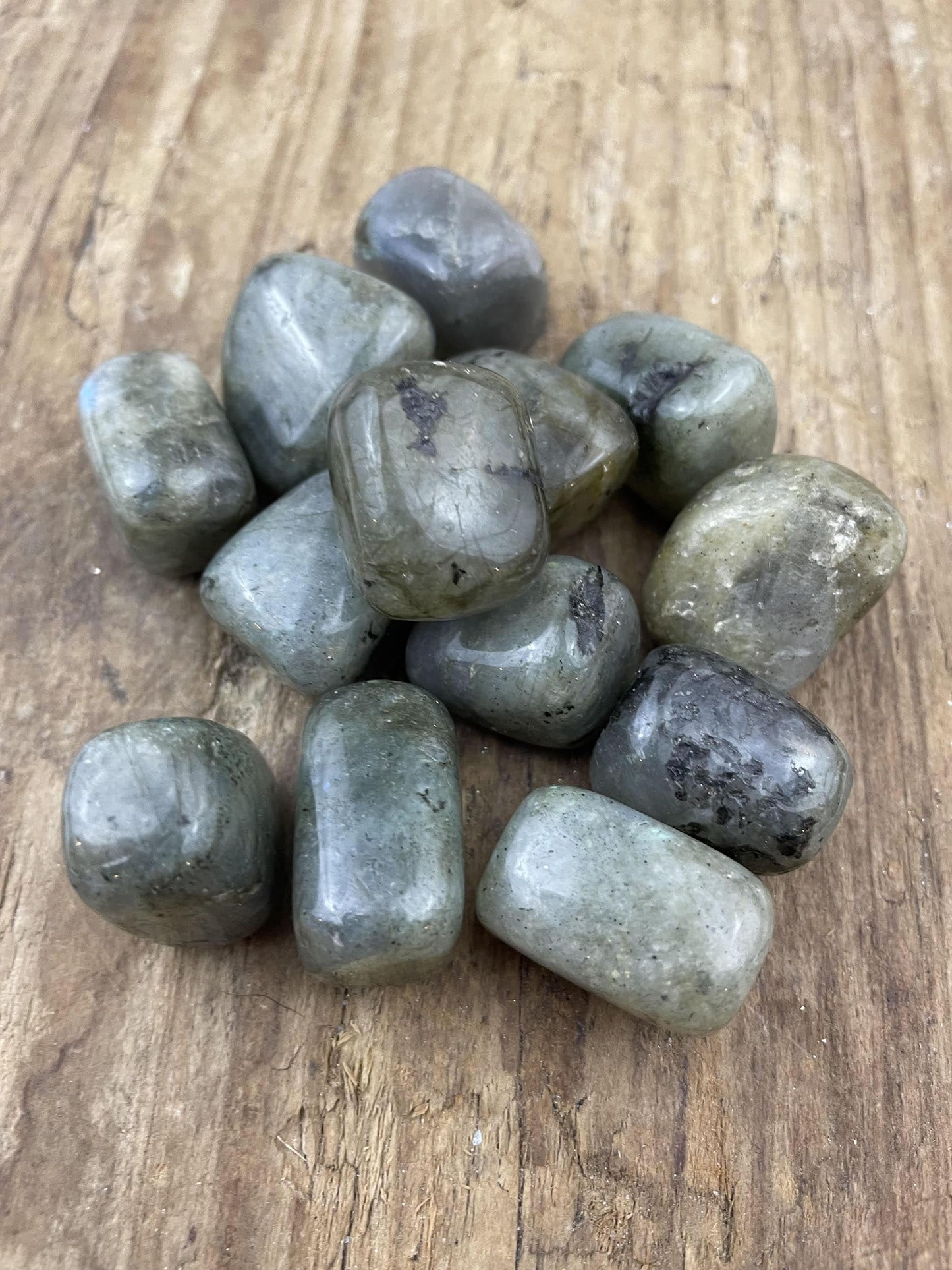 Glatte labradorit krystaller på en træoverflade, vist i en bunke i naturligt lys.