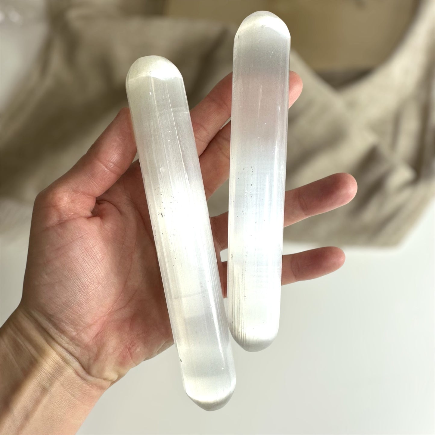 Hånd holder to runde selenit stave med en blød baggrund.