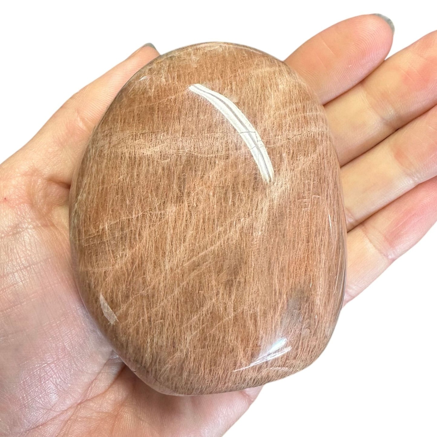 En hånd holder en glat, poleret fersken månesten i fri form med en varm, brunlig nuance.