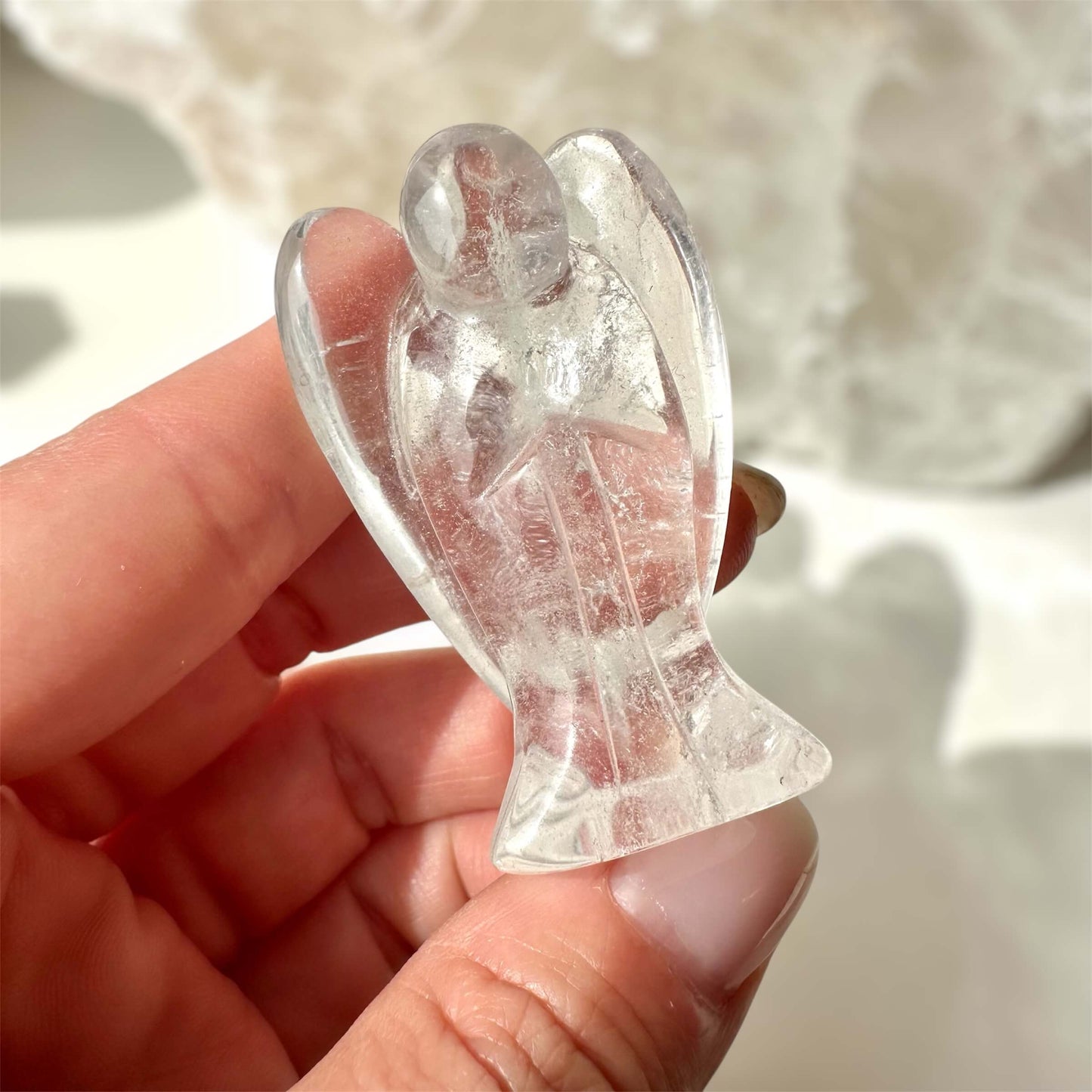 Bjergkrystal engel holdt mellem fingrene i sollys, viser gennemsigtige detaljer og lysrefleksioner.